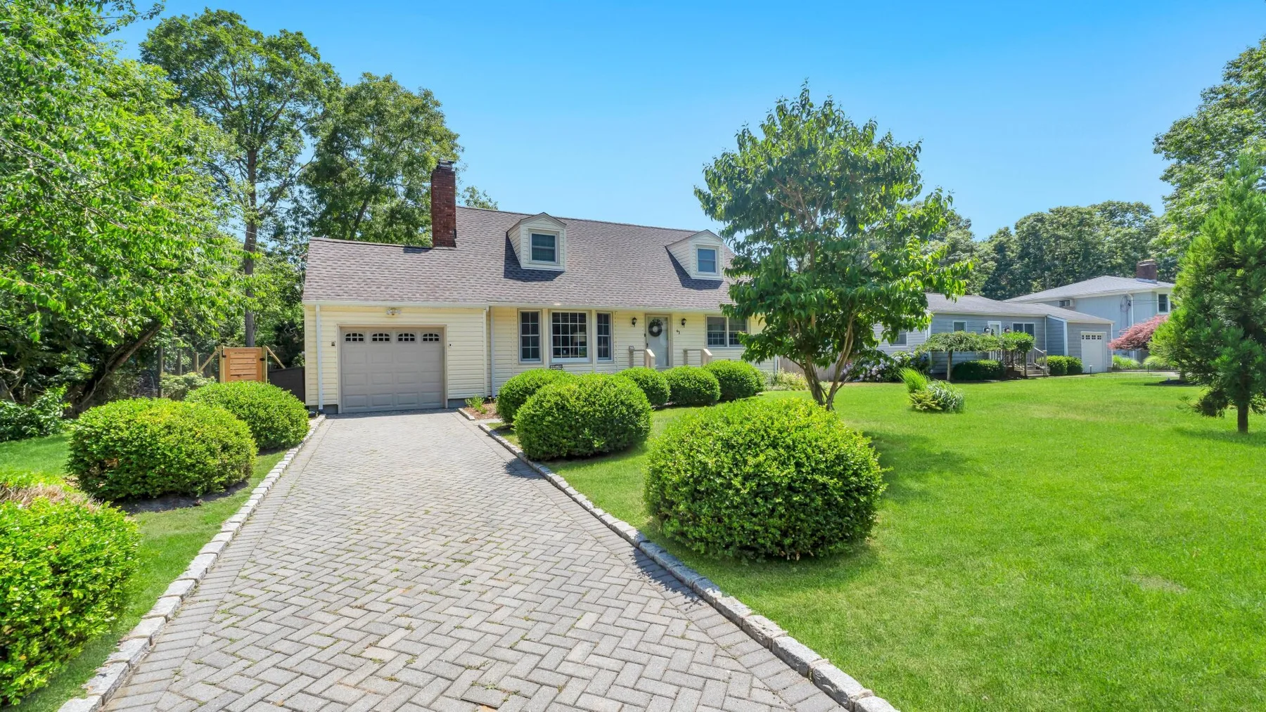 A house with a paved driveway, trimmed shrubs, and a broad green lawn.