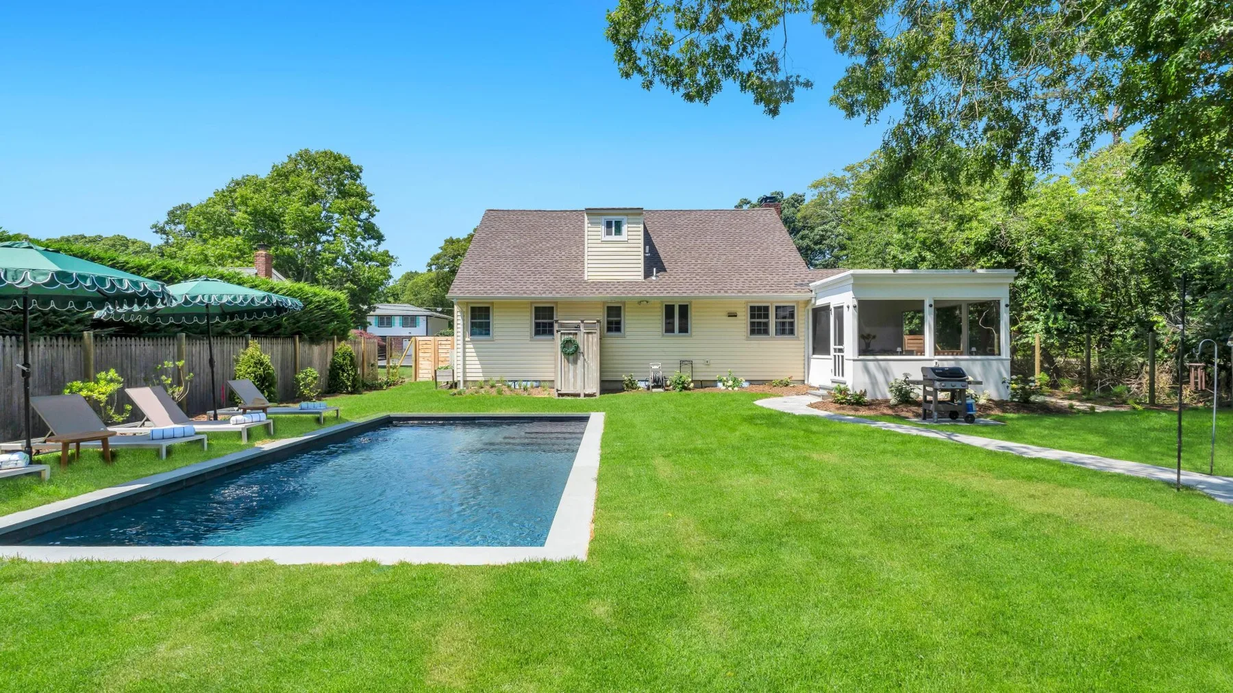 A backyard with a swimming pool, lawn, and a house.