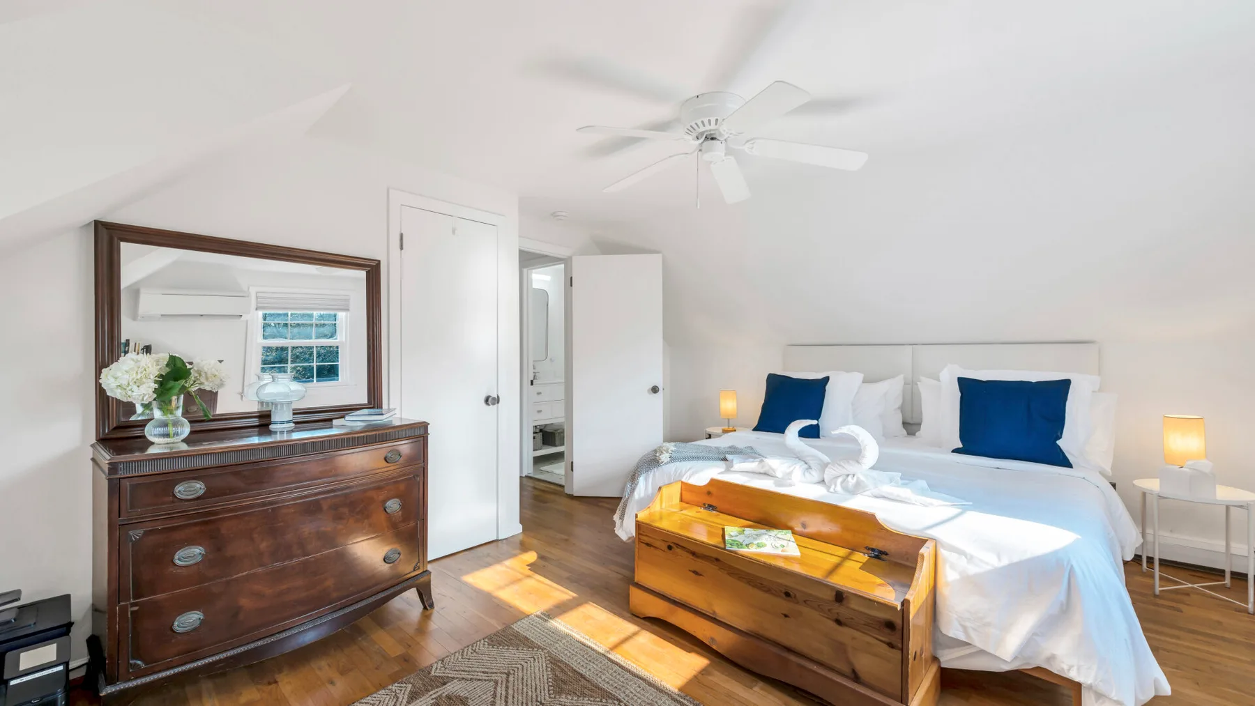 A bright bedroom with a bed, wooden dresser, and ceiling fan.