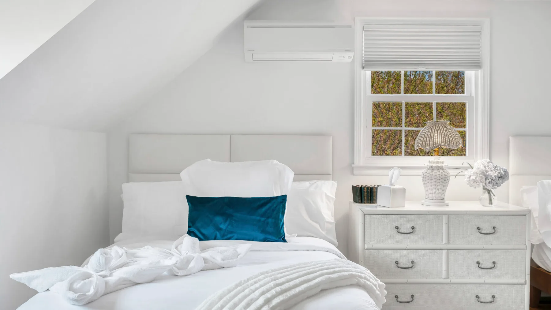 A bright bedroom with a bed, white bedding, and a dresser beneath a window.