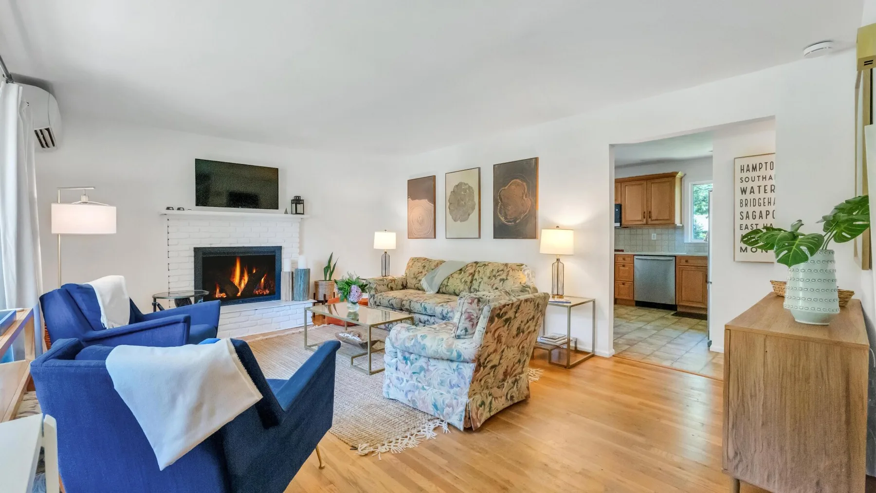 A living room with blue seating, a fireplace, and an open kitchen beyond.