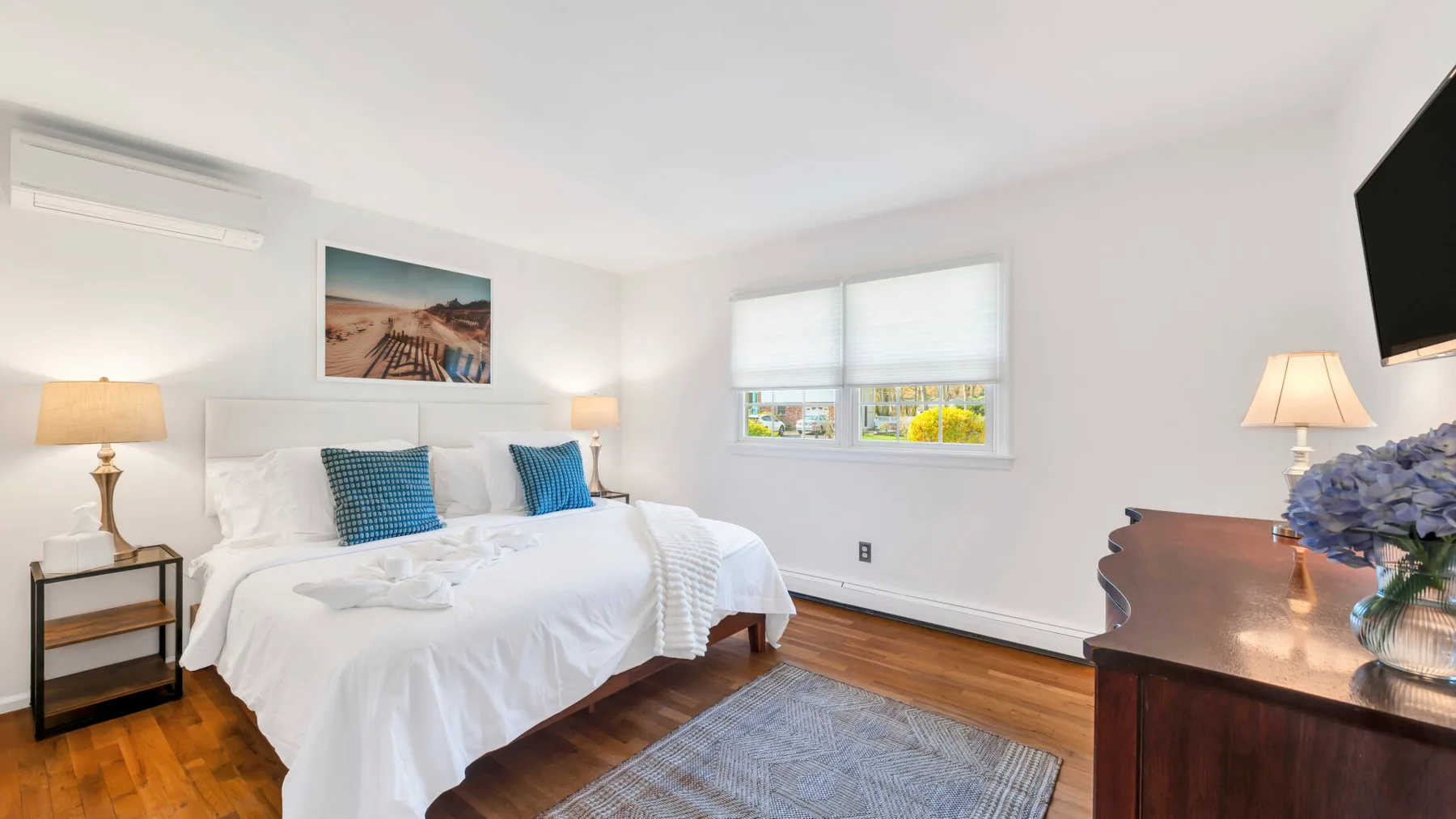 A bright bedroom with a neatly made bed and a window overlooking greenery.