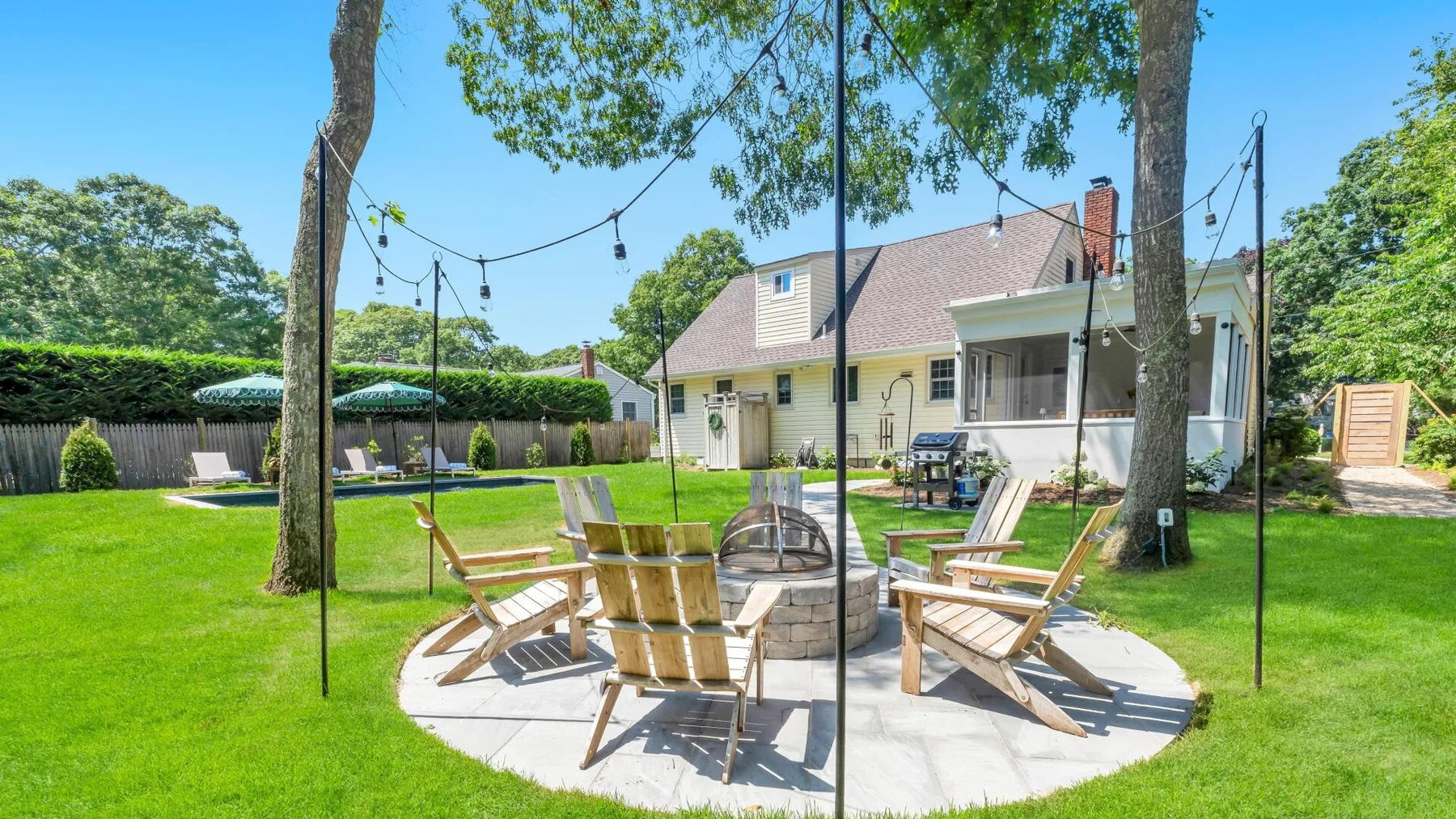 A grassy backyard patio with outdoor seating beneath string lights.