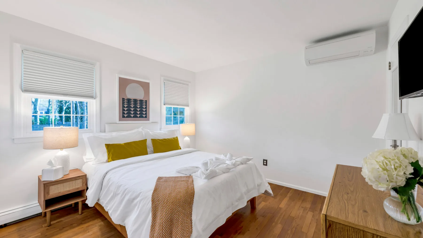 A bright bedroom with a neatly made bed, two windows, and bedside lamps.