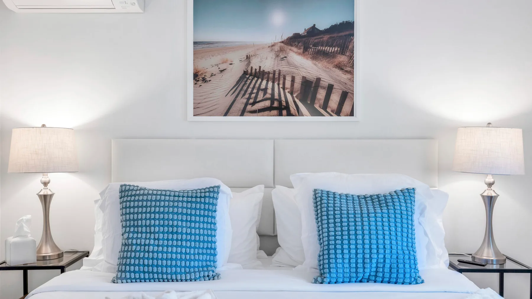 A bedroom with a double bed, blue accent pillows, and matching bedside lamps.