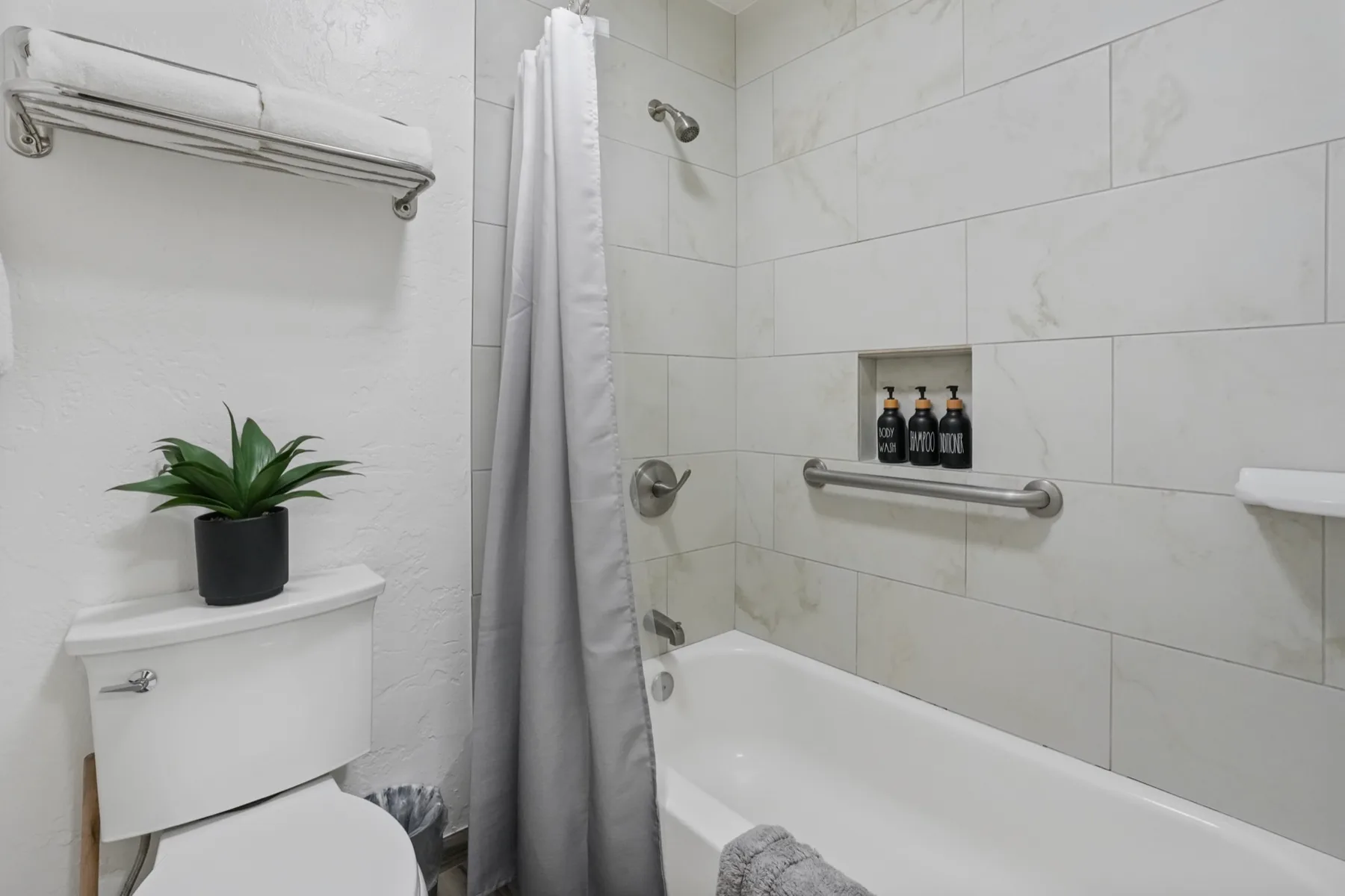 Un baño con azulejos, bañera, cortina de ducha y una pequeña planta en maceta.