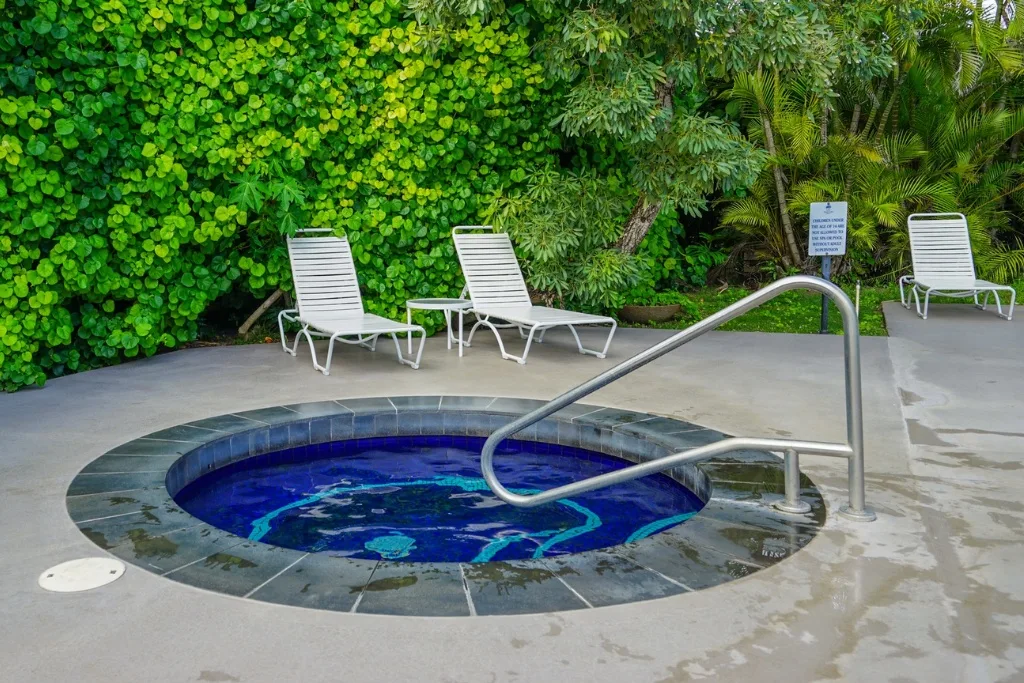 Una pequeña piscina redonda está junto a asientos reclinables y vegetación frondosa.