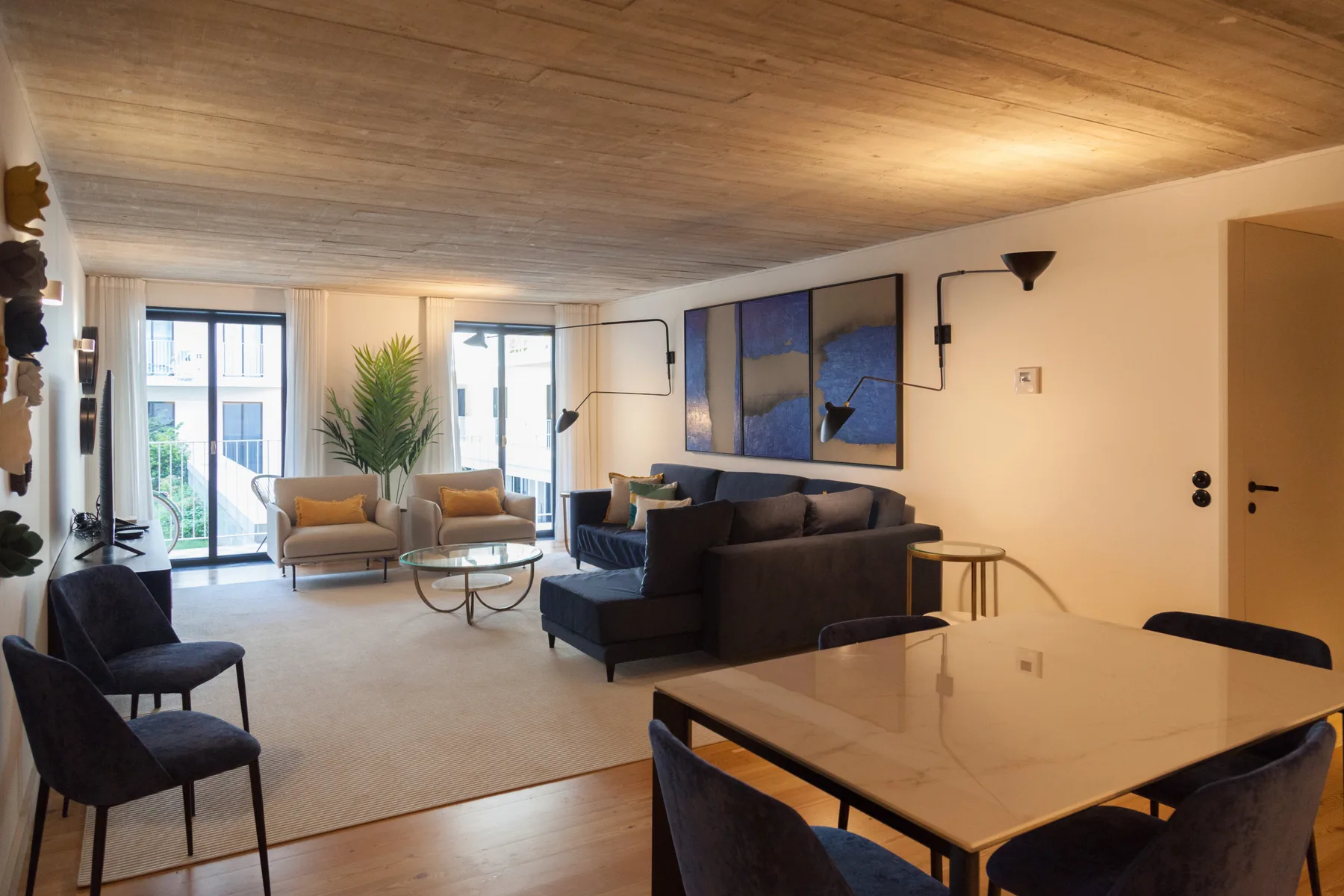 Sala de estar y comedor con asientos, una mesa y grandes ventanas.