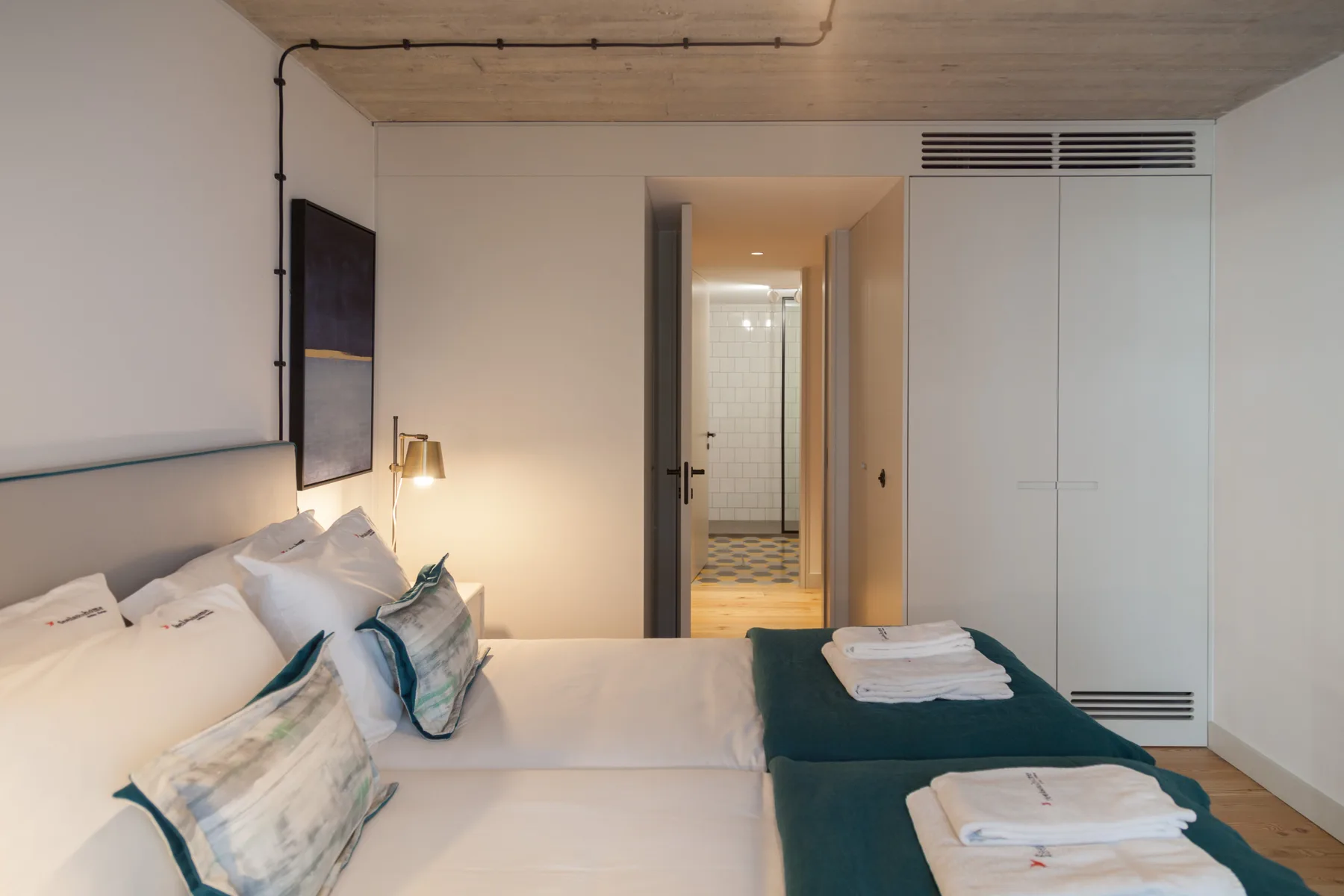 Un dormitorio con una cama, toallas dobladas y una puerta abierta a un baño con azulejos.