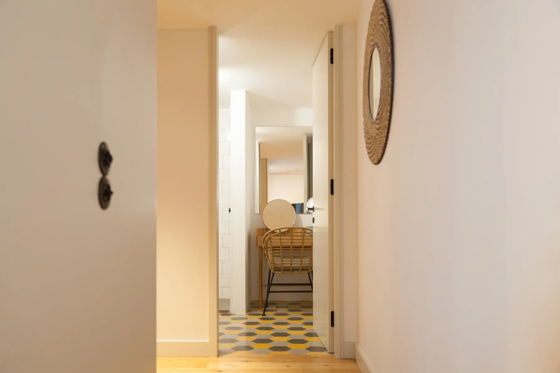 Un pasillo luminoso conduce a una habitación con una silla tejida y suelo estampado.