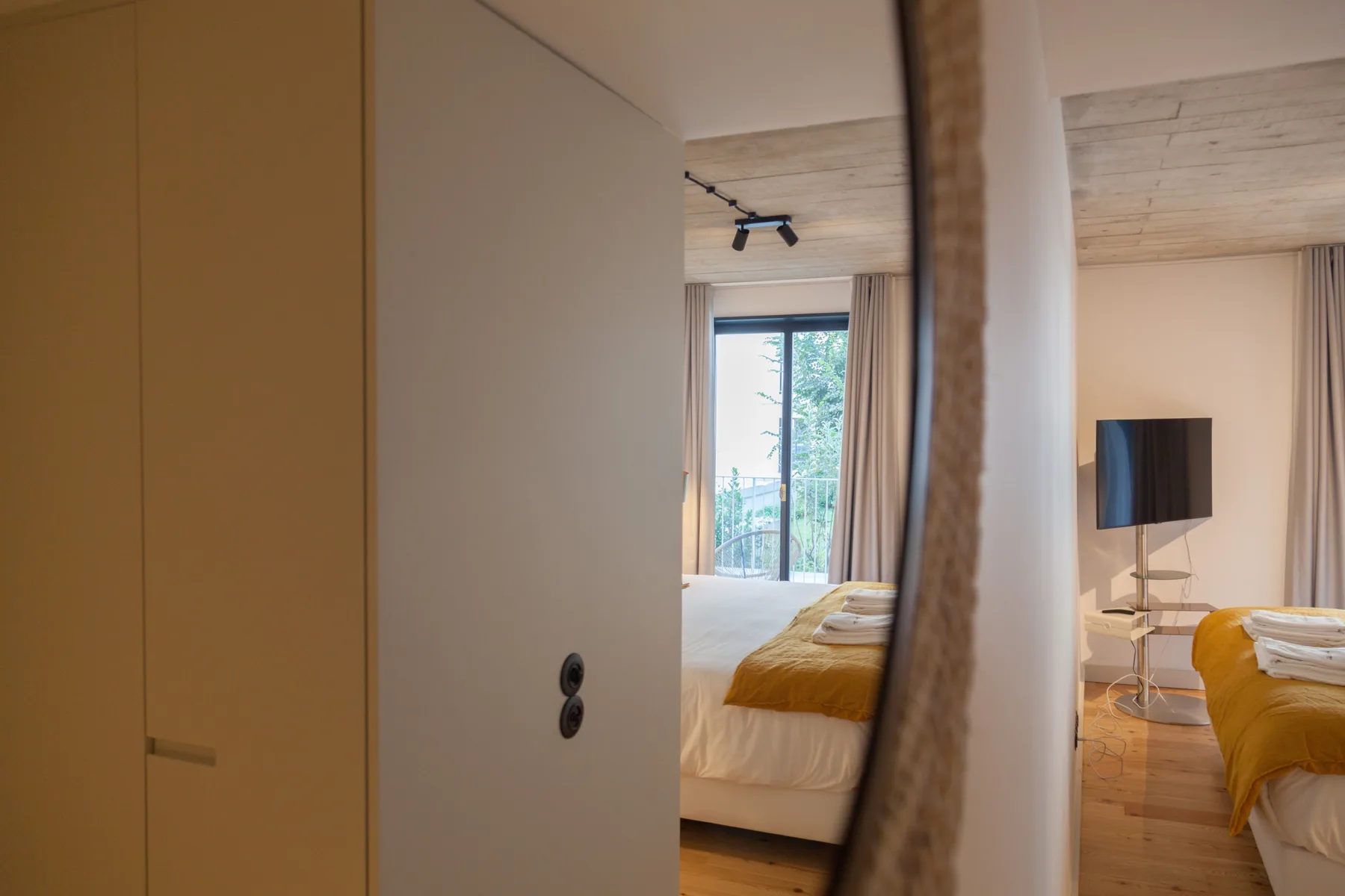 Un dormitorio con una colcha amarilla y un televisor visible en la zona contigua.