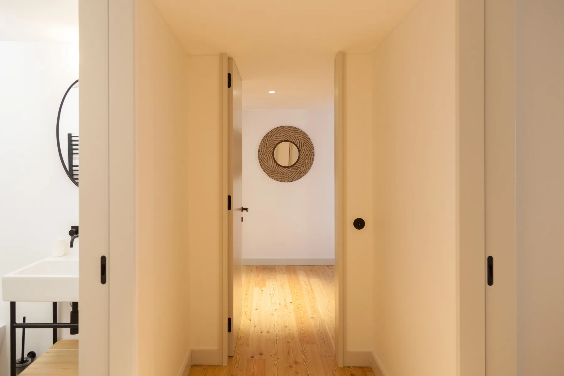 Un pasillo conduce a una habitación luminosa con un espejo circular en la pared del fondo.