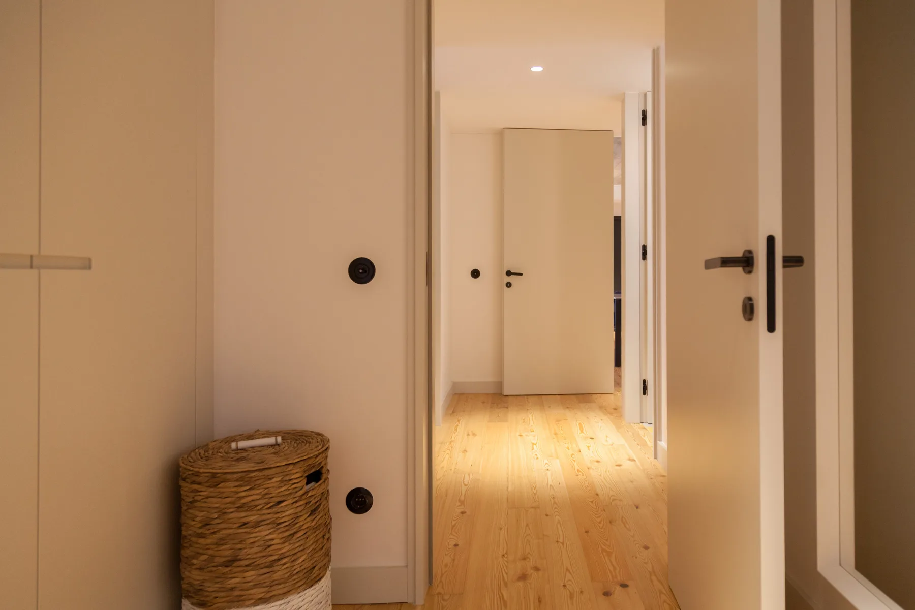 Un pasillo luminoso con suelo de madera clara y puertas interiores abiertas.