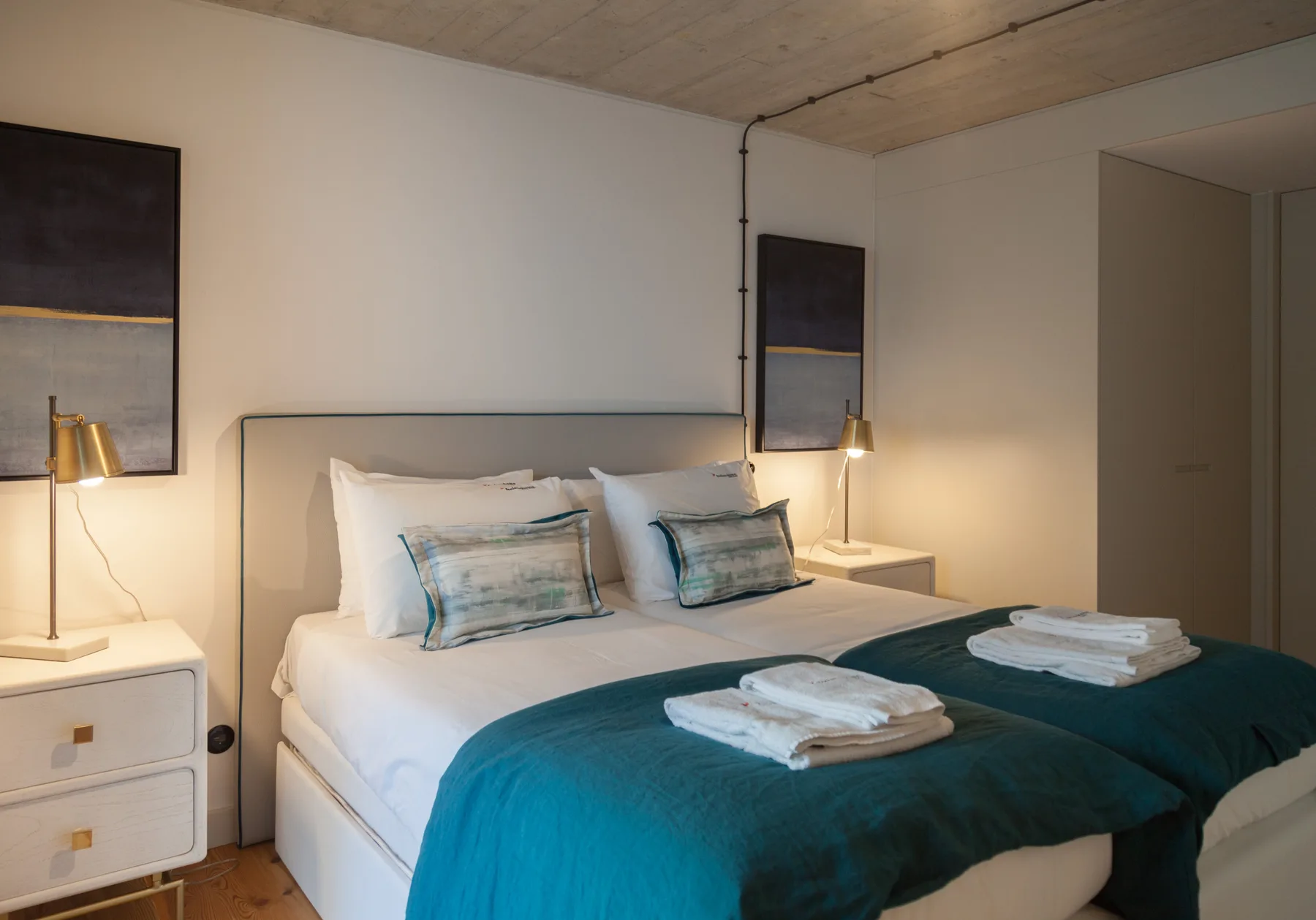 Un dormitorio con una cama vestida con sábanas blancas y una colcha verde azulado.