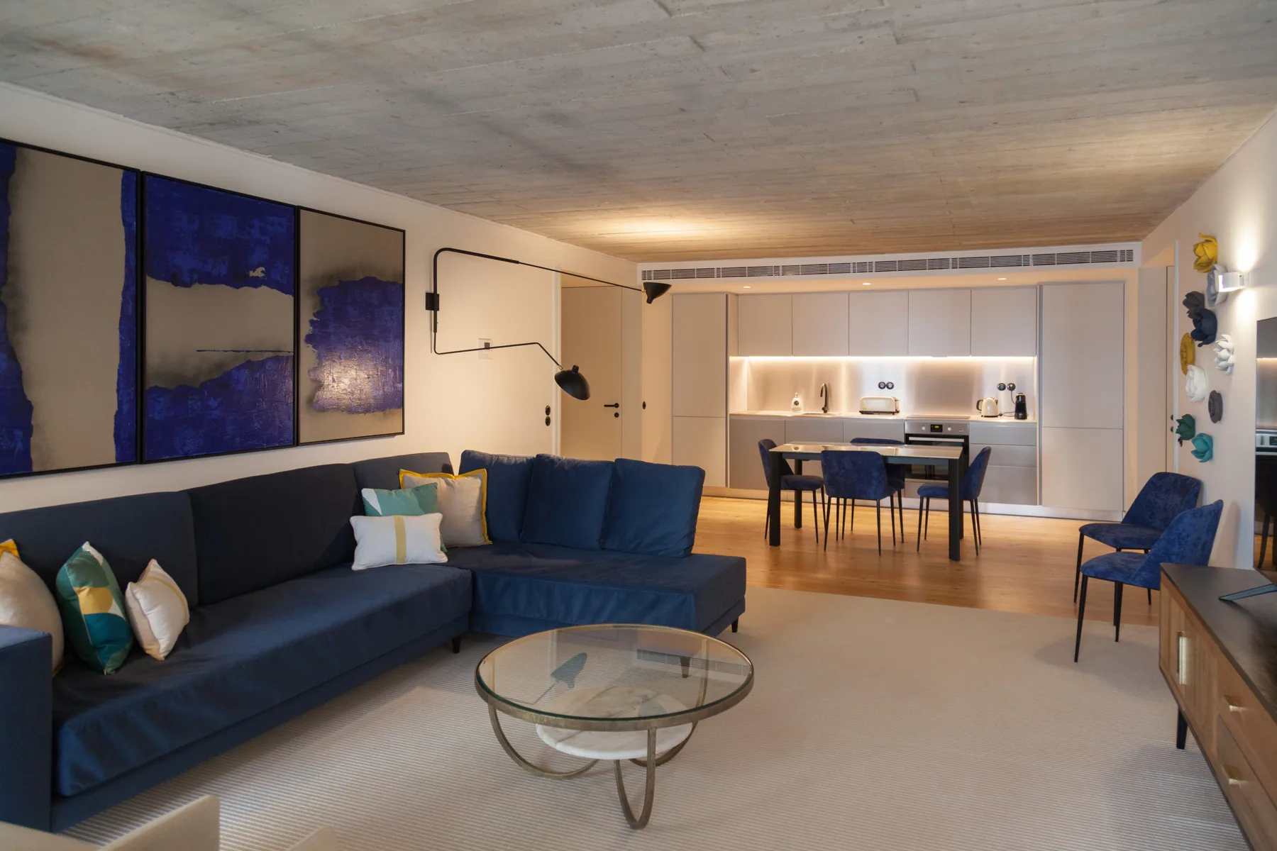 Una sala de estar con asientos azules se abre a un comedor y una cocina.