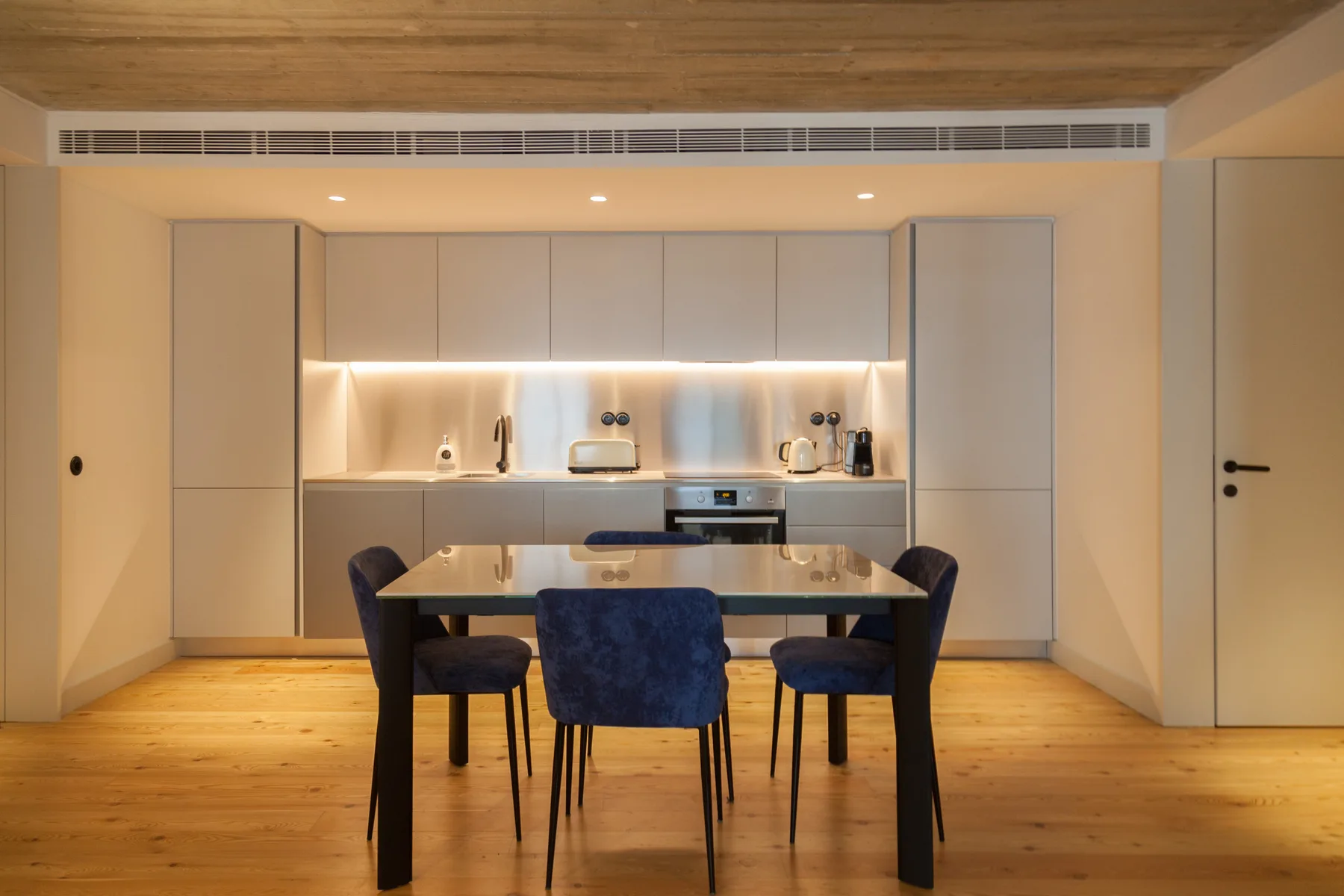 Un comedor con una mesa y sillas frente a una cocina moderna.