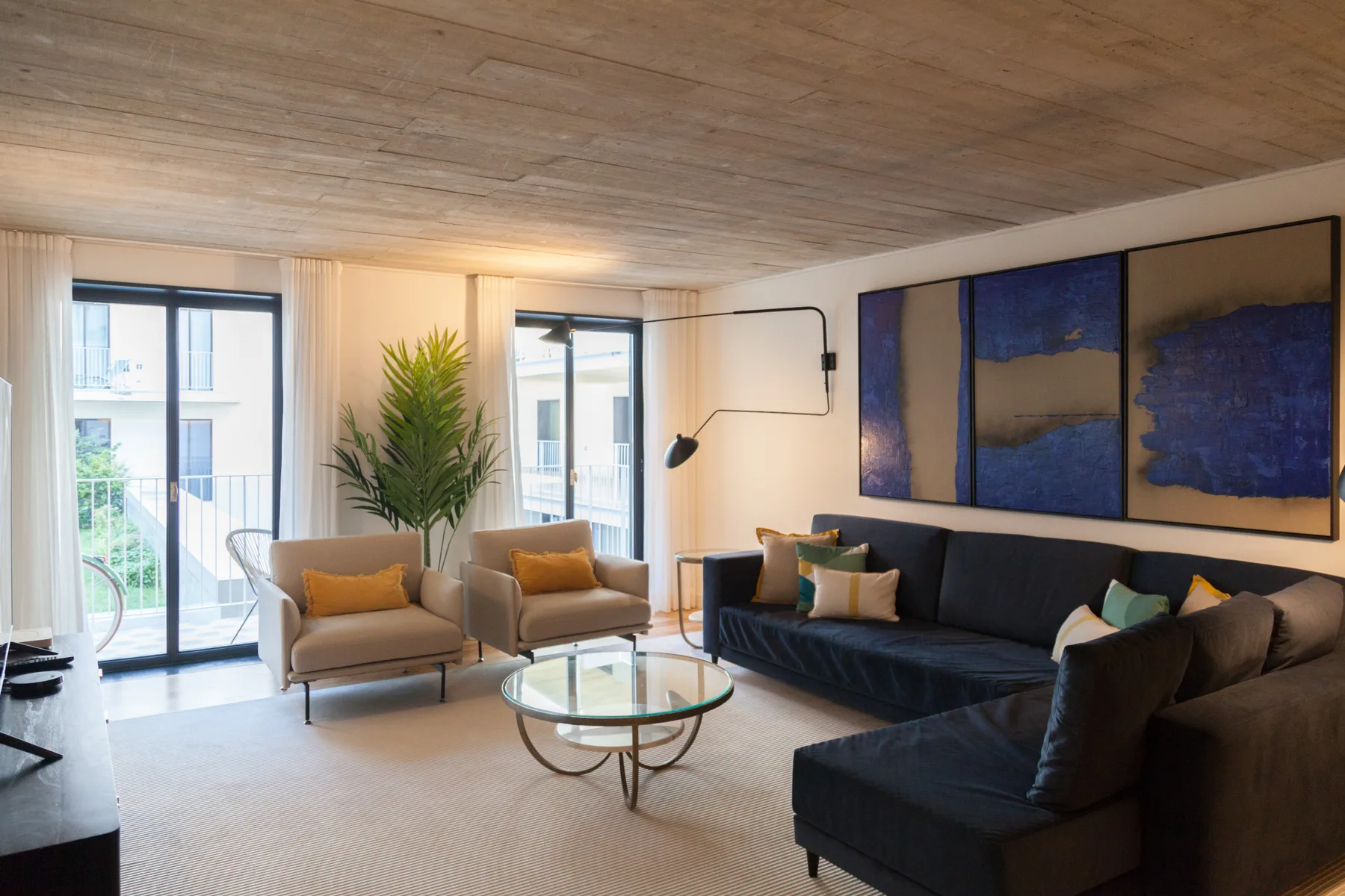 Una sala luminosa tiene asientos, una mesa de centro de vidrio y ventanas grandes.