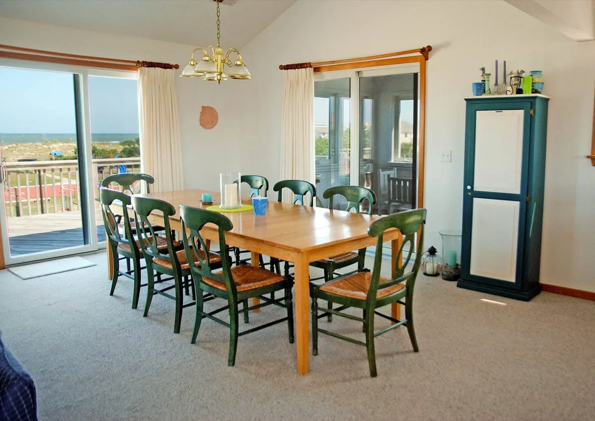 Comedor con una mesa de madera y sillas verdes junto a grandes ventanales.