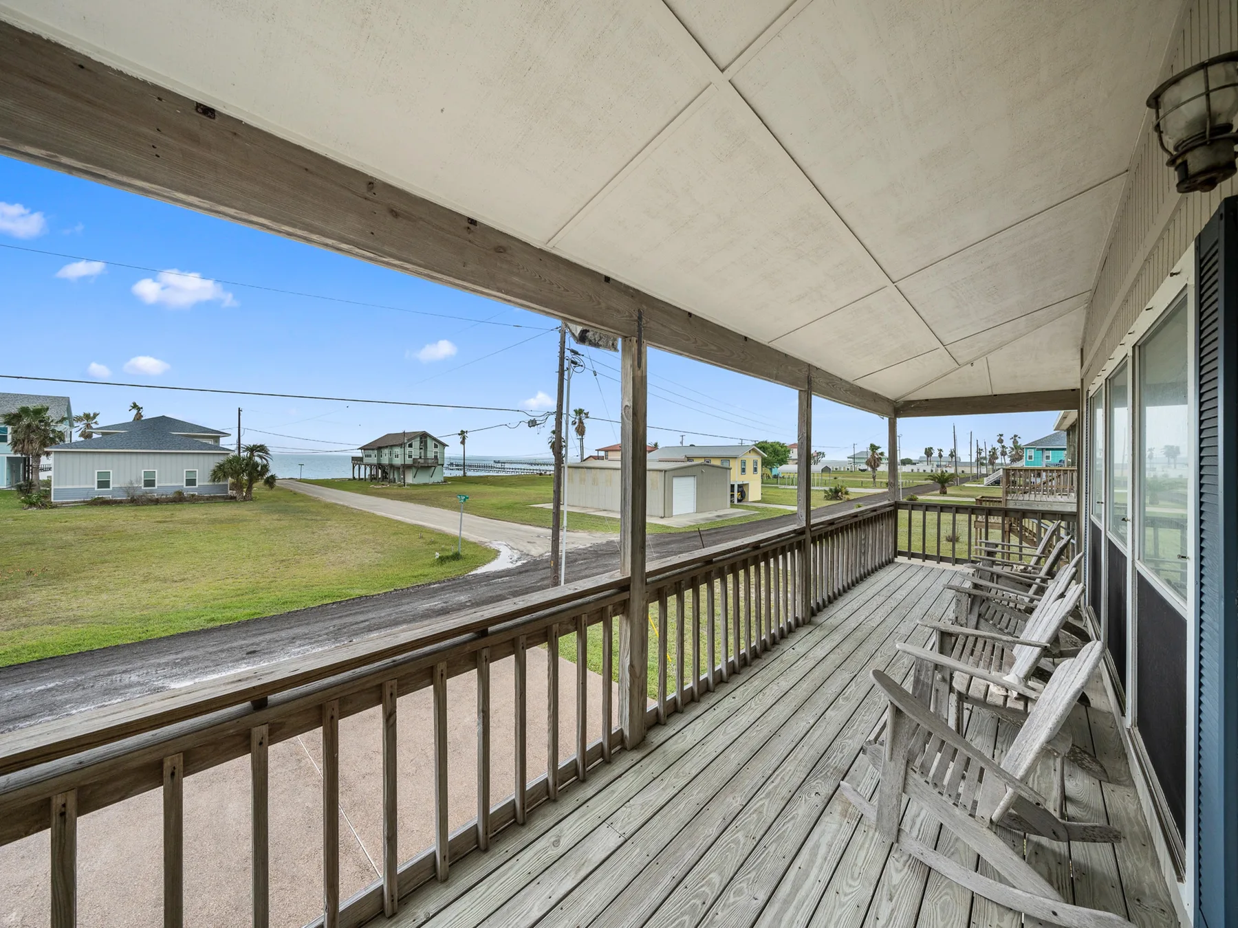 A covered porch with wooden seating overlooks a grassy neighborhood.
