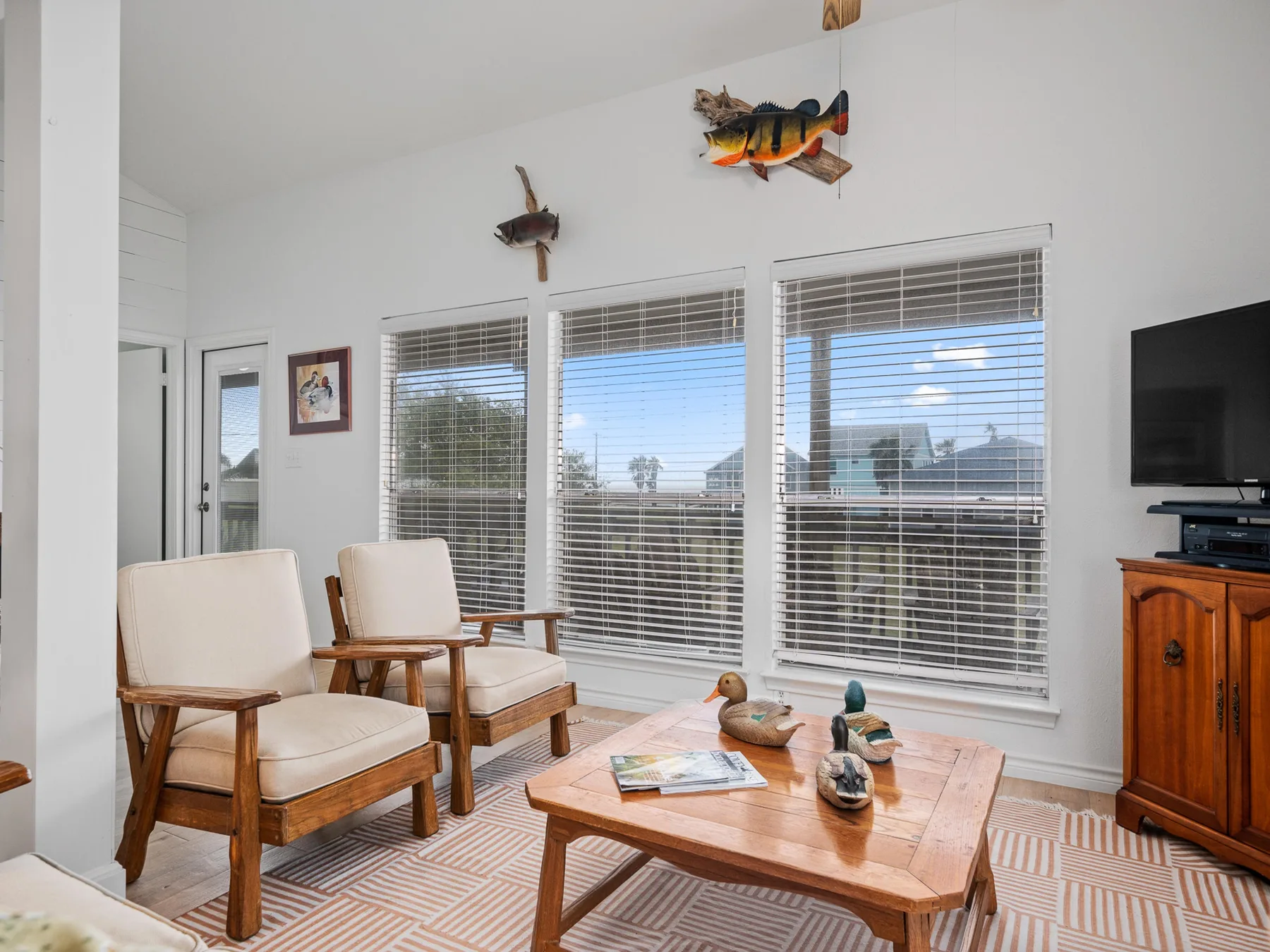 A bright living room has large windows, seating, and a wooden coffee table.