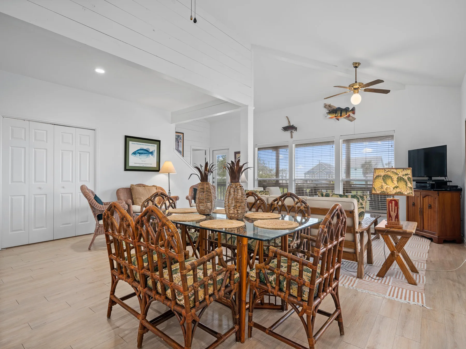 A dining area with wicker seating around a table beside large windows.