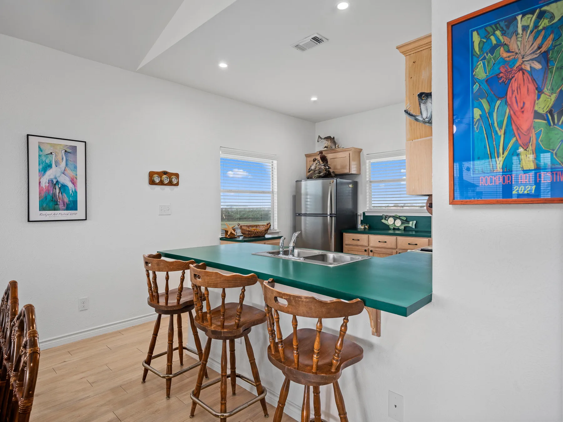 A bright kitchen with a green island, wooden stools, and stainless-steel appliances.