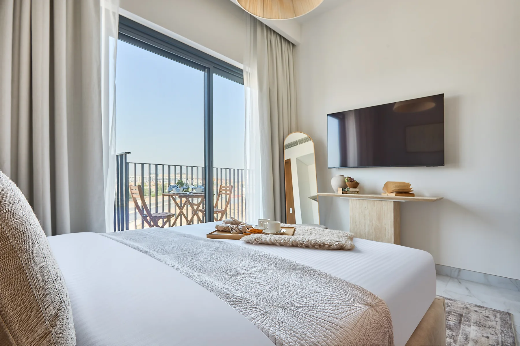 A bright bedroom with a neatly made bed beside a large glass door.