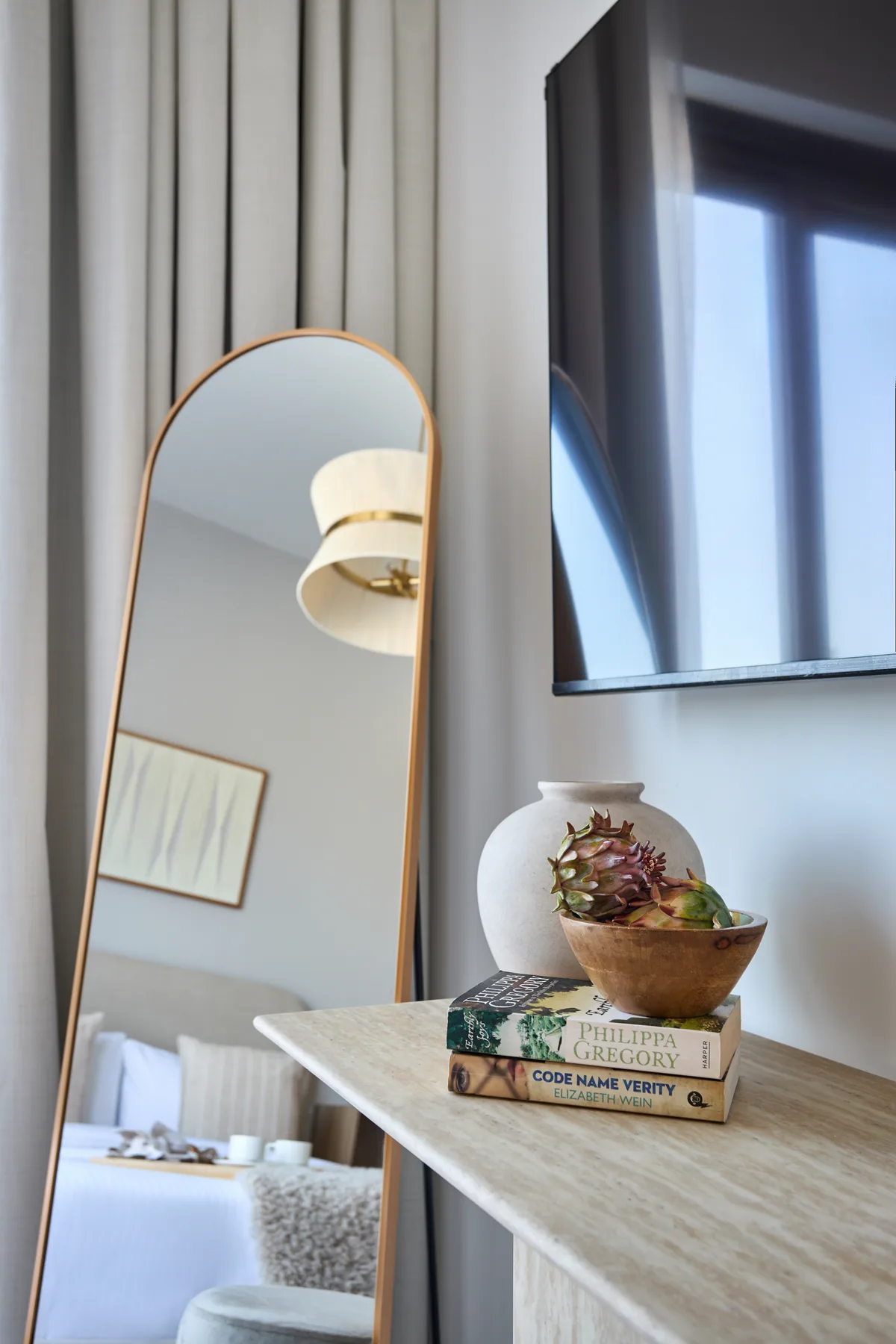 A bedroom with a tall mirror, a wall-mounted television, and a bedside table.