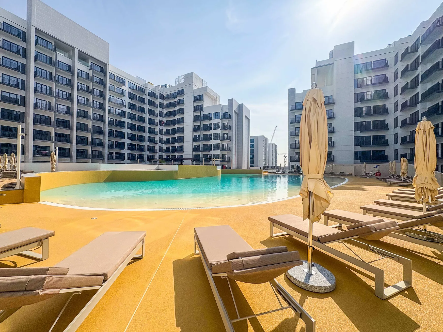 An outdoor pool surrounded by loungers and modern apartment buildings.