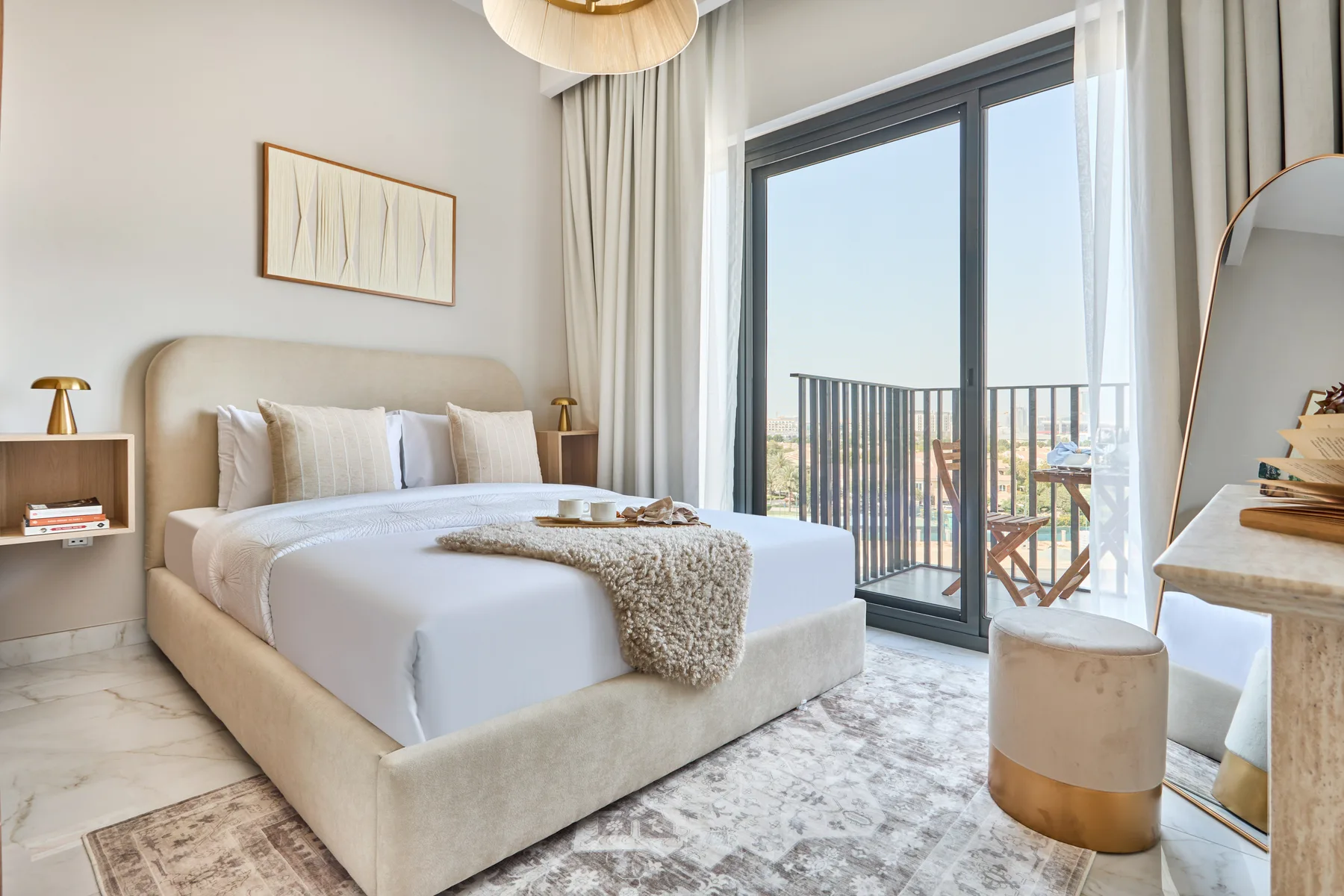 A bright bedroom with a neatly made bed beside a large window and balcony.