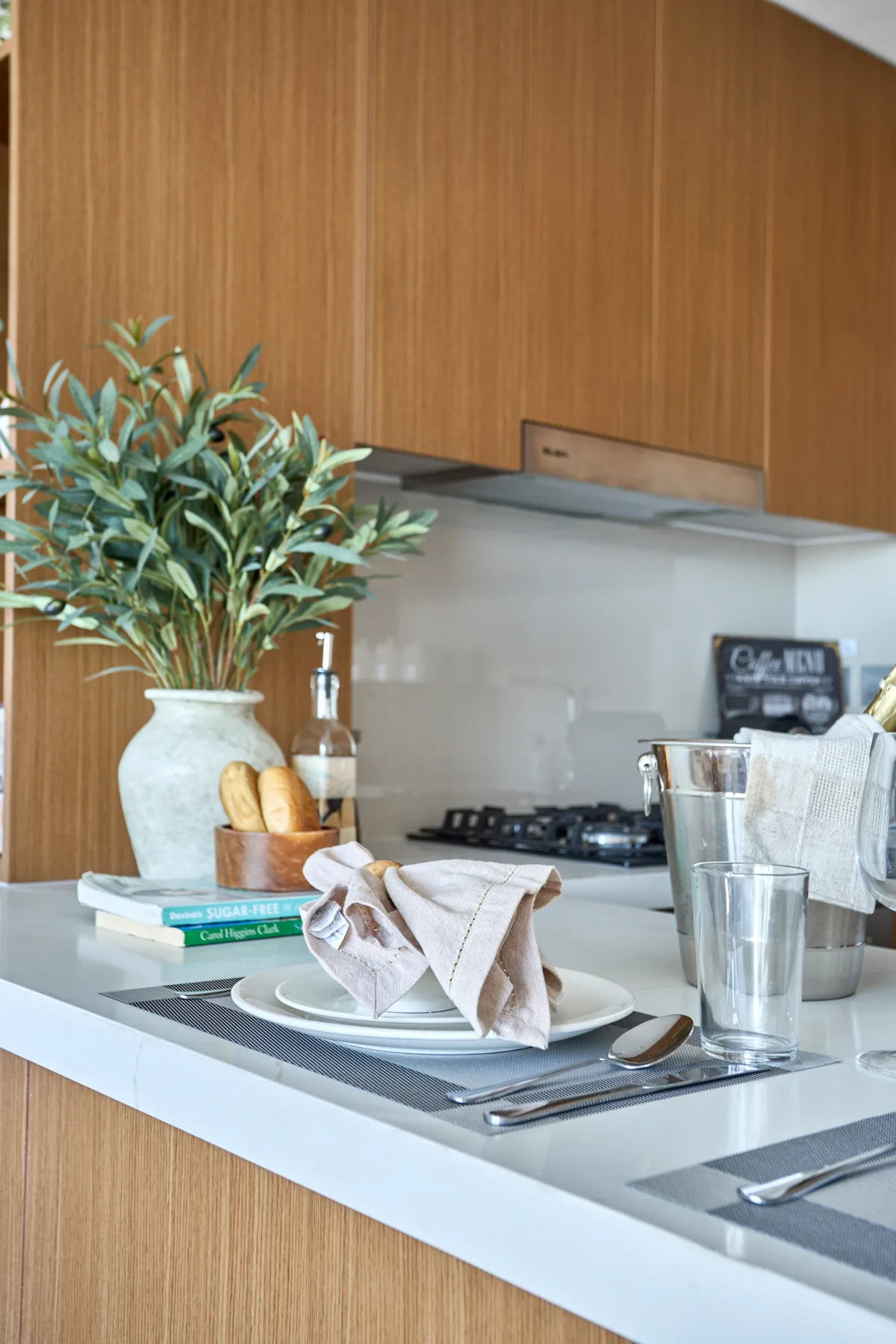 A kitchen counter with wooden cabinets, place settings, and a leafy plant.
