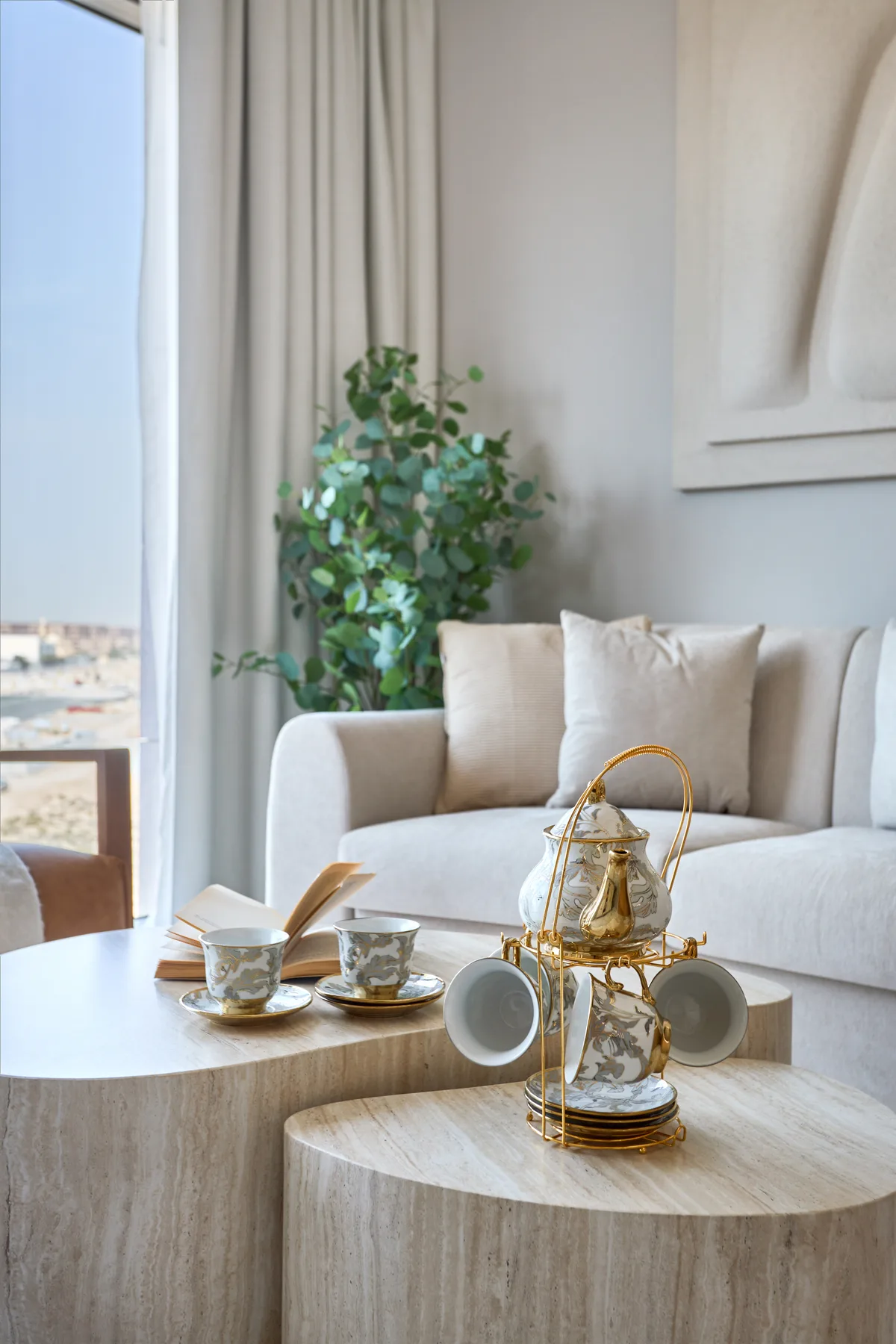 A bright living room with pale seating, a plant, and round coffee tables.