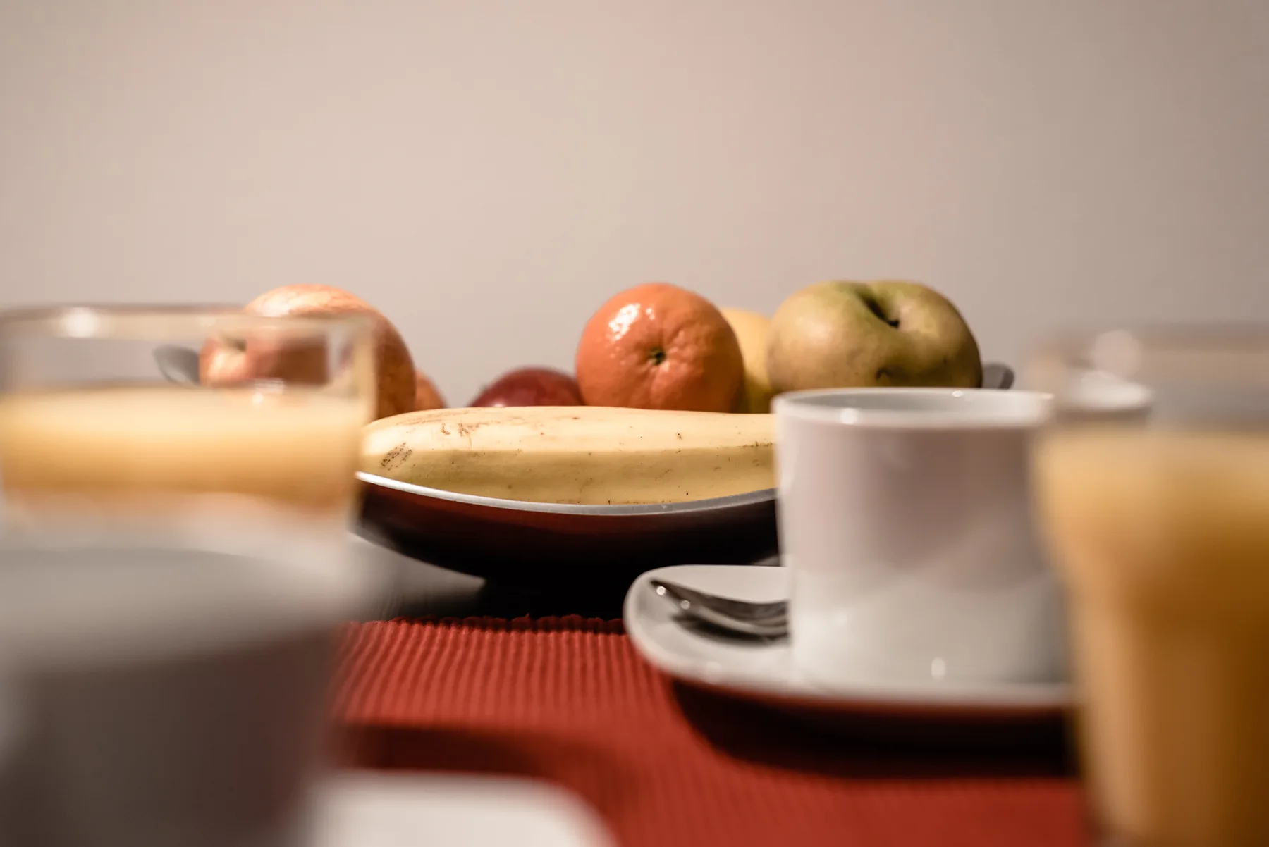 A dining table is set with cups and a plate of fruit.