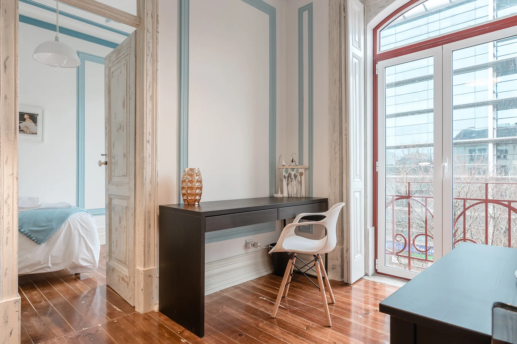 Un escritorio y una silla están junto a una ventana alta y arqueada en una habitación luminosa.
