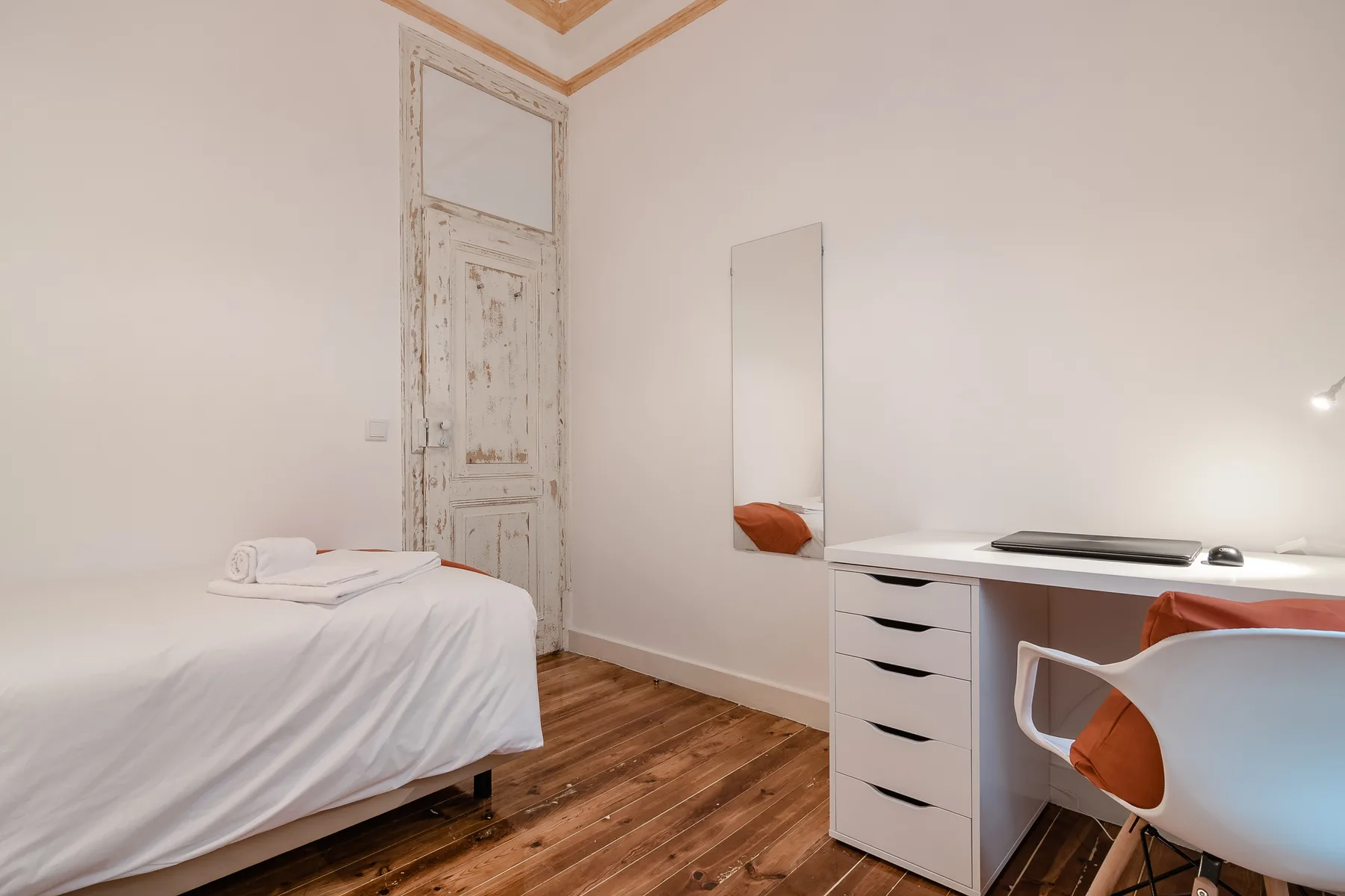 A bedroom with a bed and a desk beside a tall mirror.