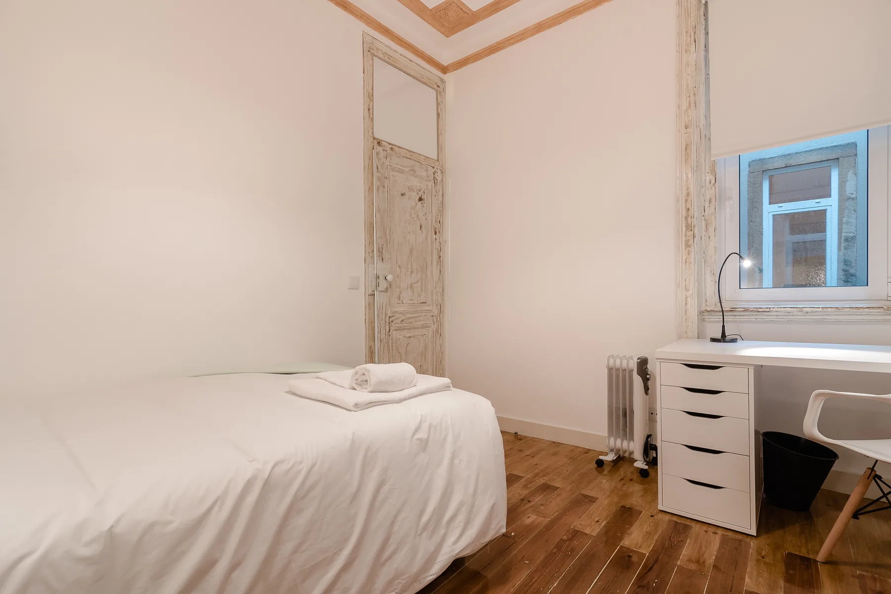 A bedroom with a bed, a desk, and a window.