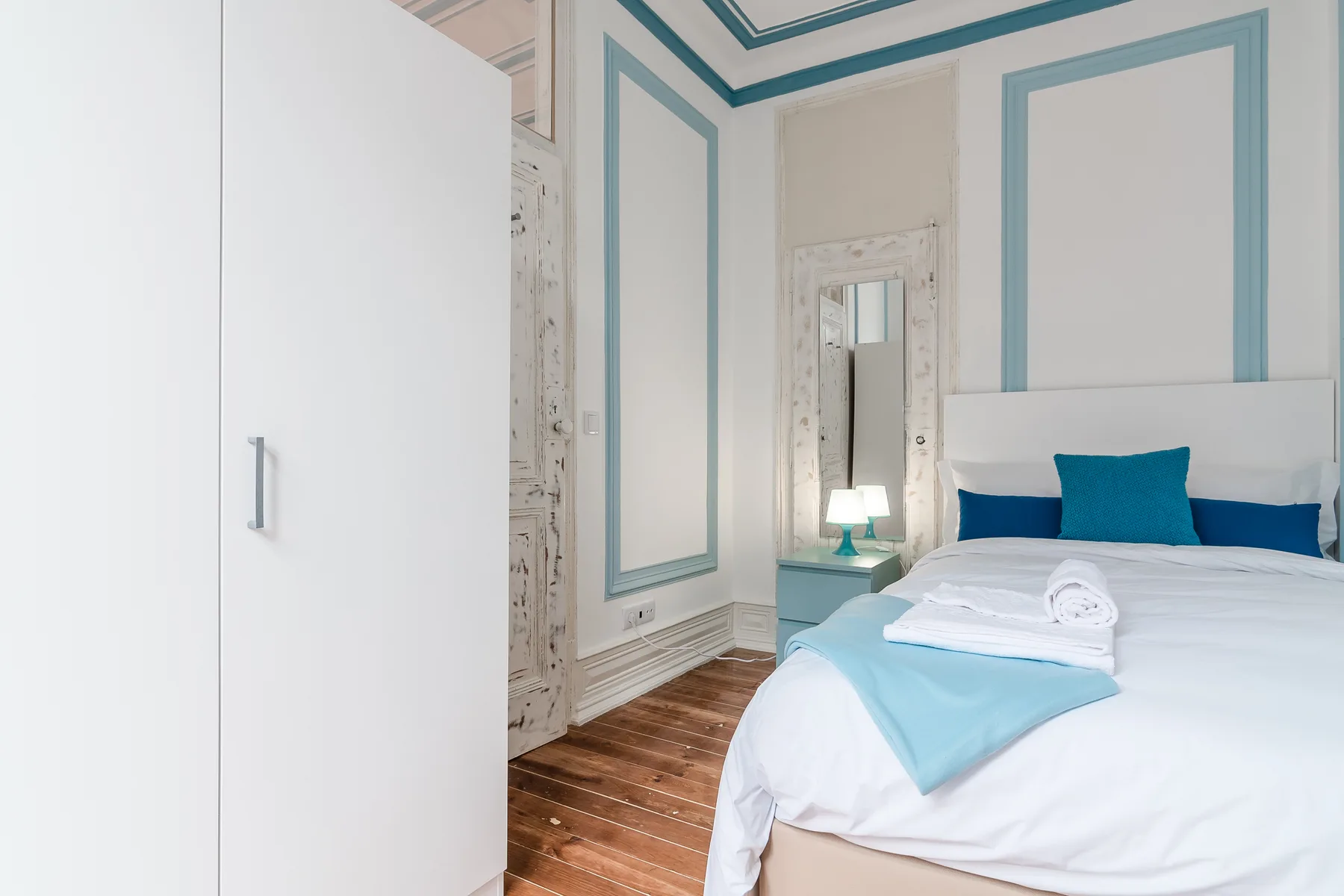 A bright bedroom with a neatly made bed and teal wall trim.