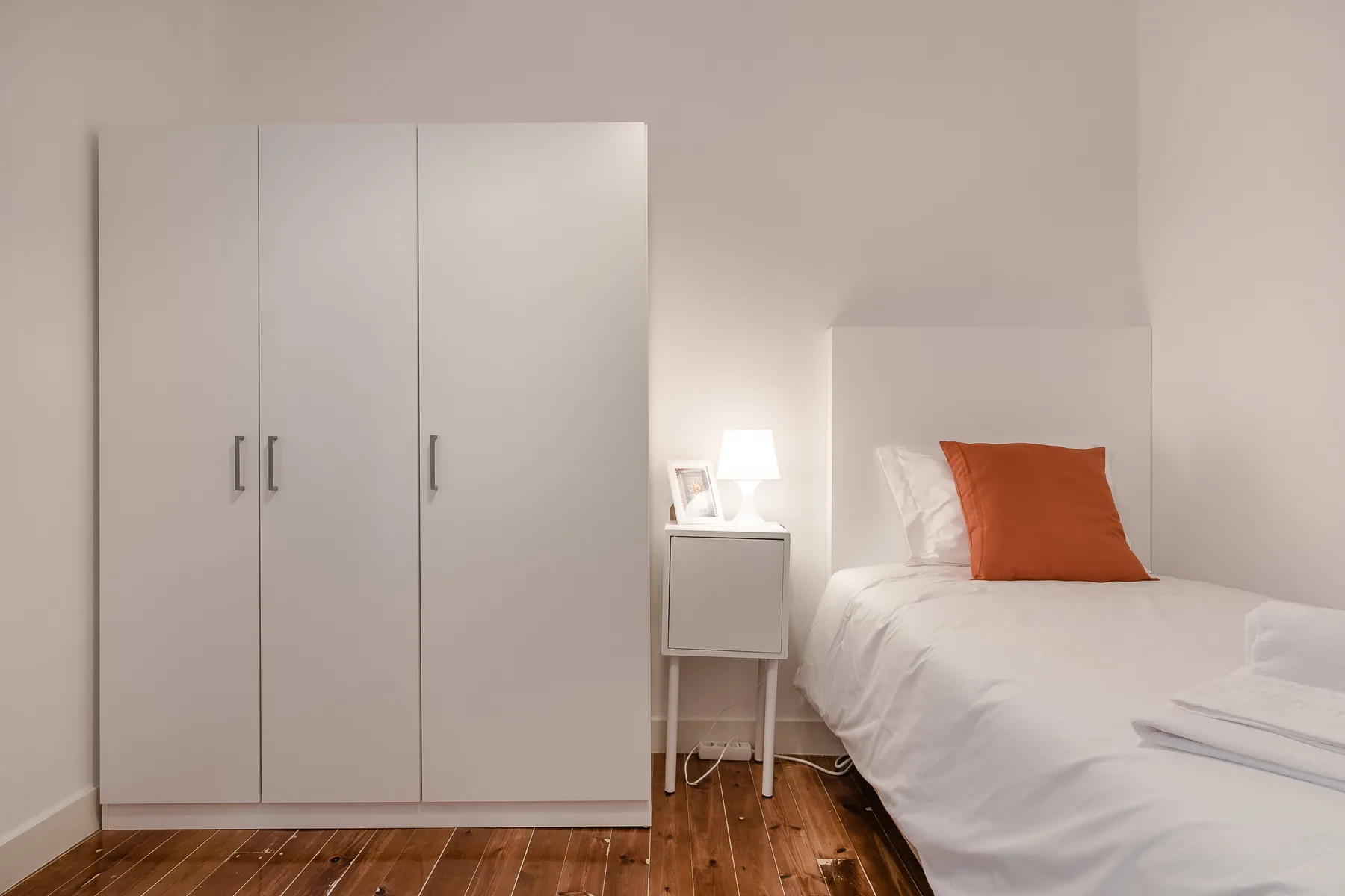 A bedroom with a bed, white wardrobe, and bedside table.