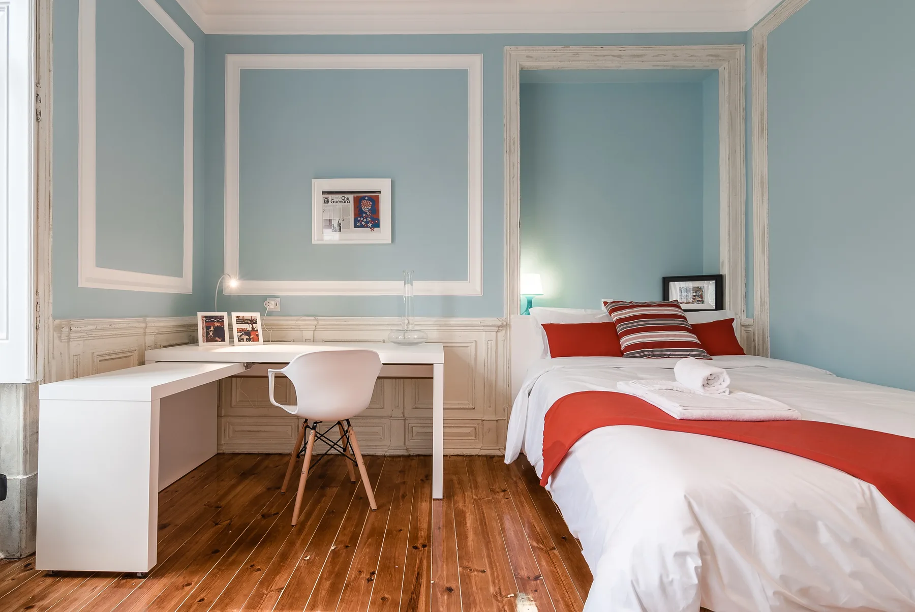 A bedroom with a bed and a desk against pale blue paneled walls.