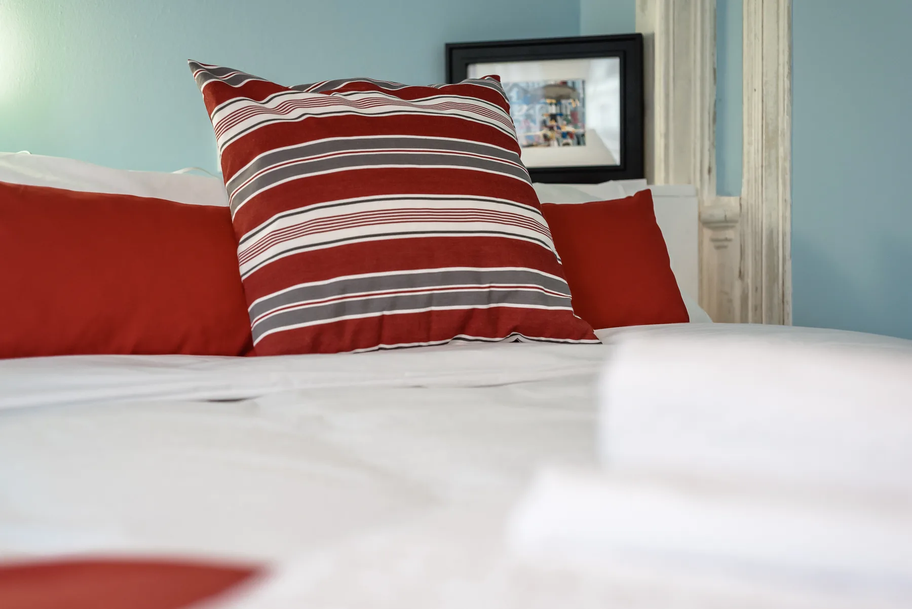A bed with red and striped pillows sits against a pale blue wall.