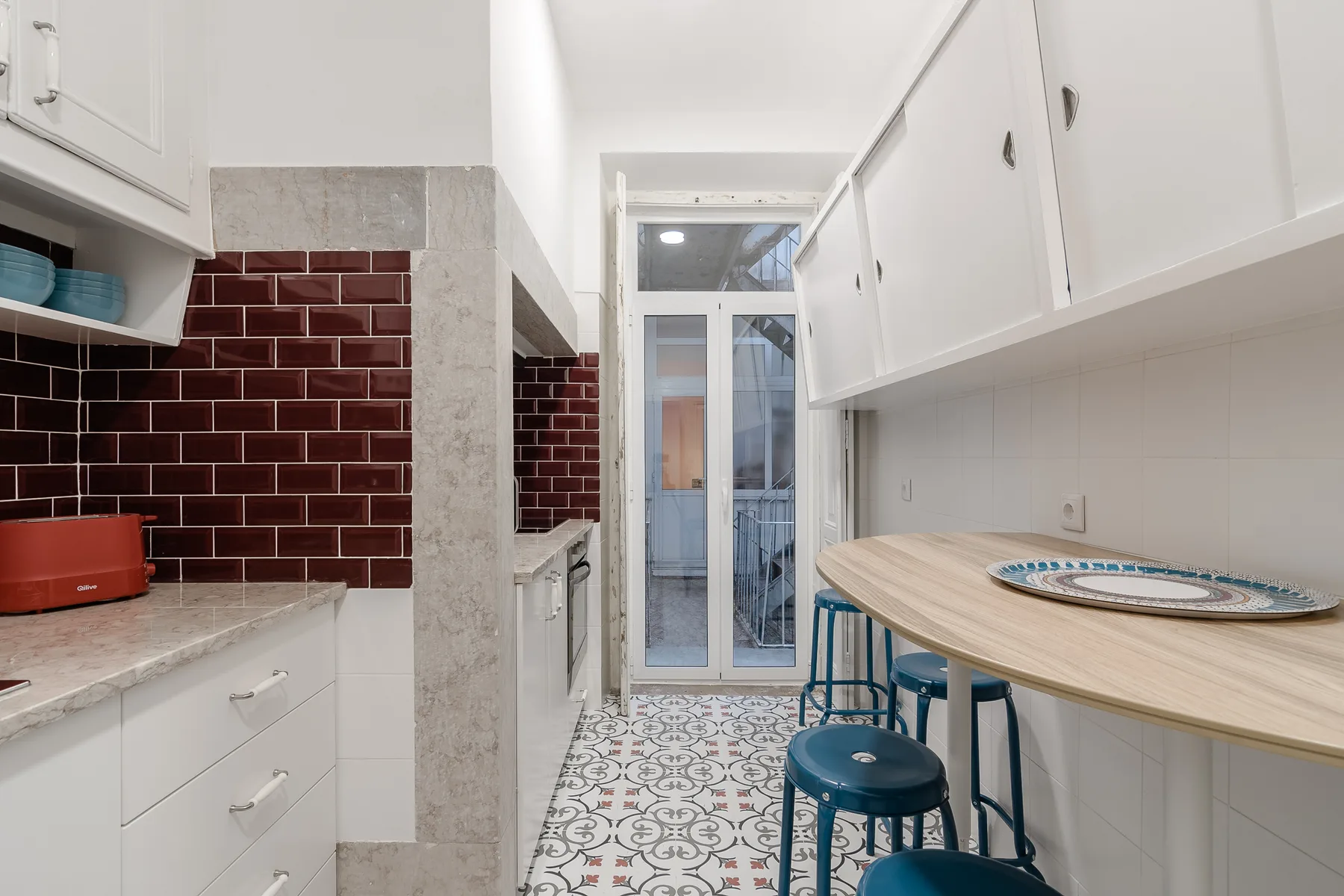 A narrow kitchen with a dining counter and patterned tile floor.