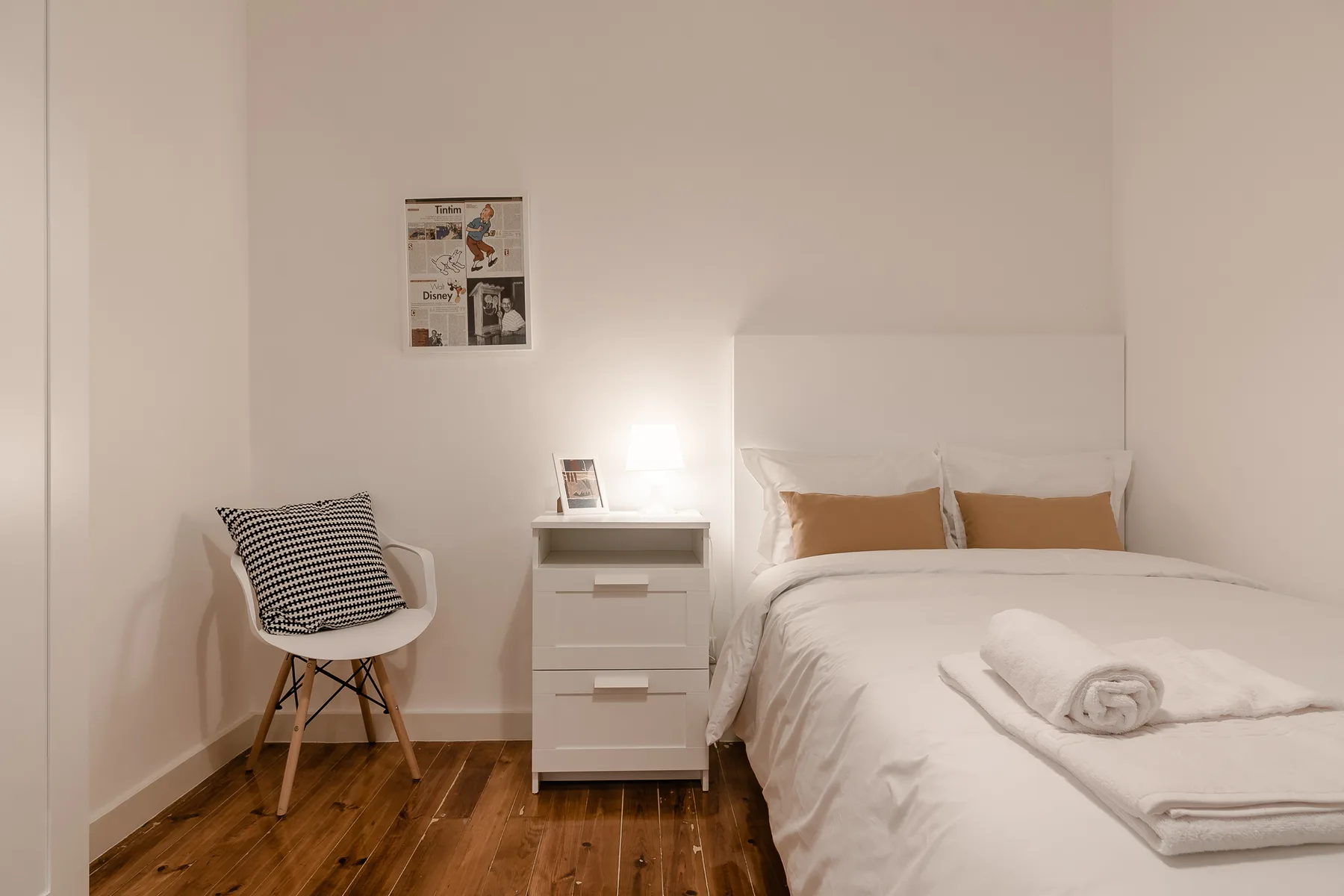 A bedroom with a neatly made bed, folded towels, and a small bedside table.