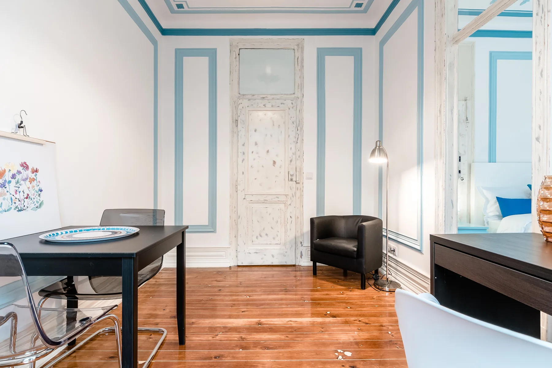 A bright dining and sitting area features a table, armchair, and ornate door.