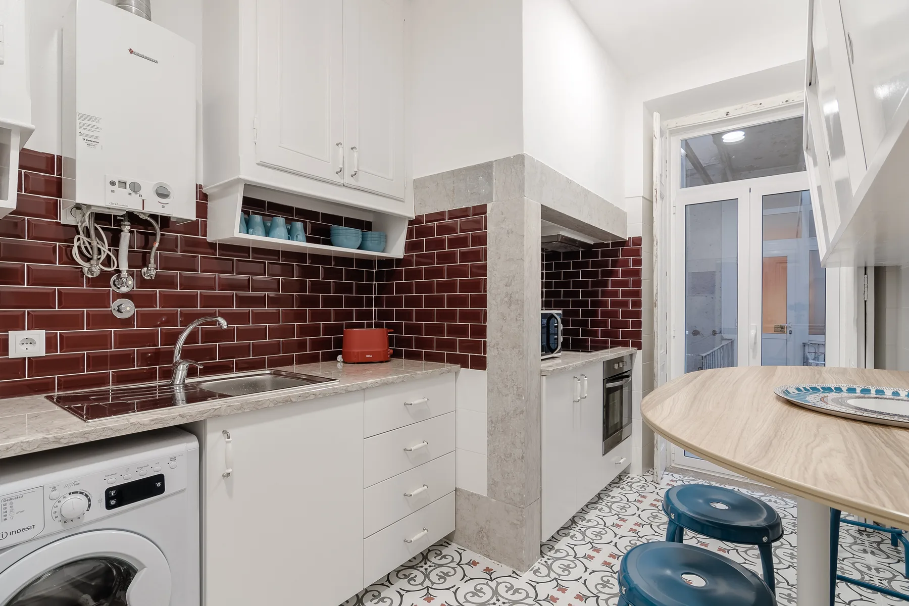 Una cocina compacta con gabinetes blancos, un salpicadero de azulejos y una mesa redonda.