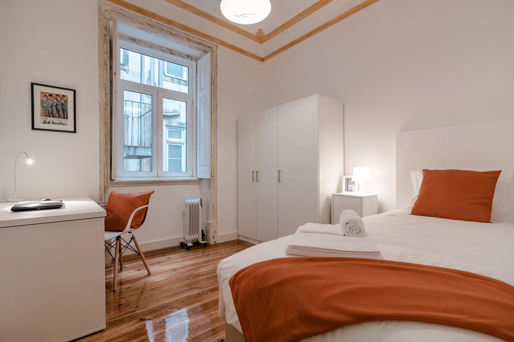 A bedroom with a bed, white wardrobe, and a small desk beside the window.