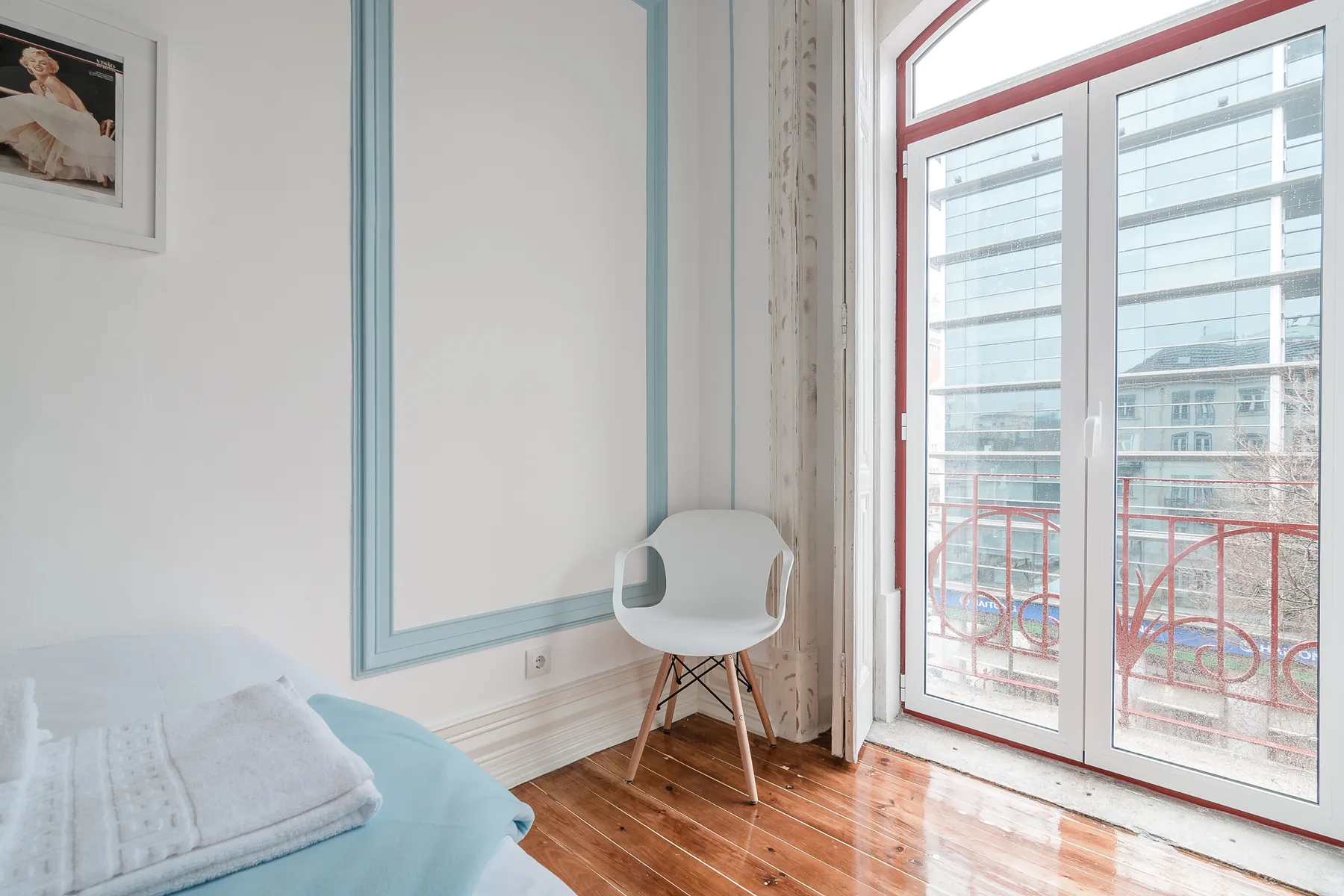 A bedroom with a white chair beside a large glass door opening onto a balcony.