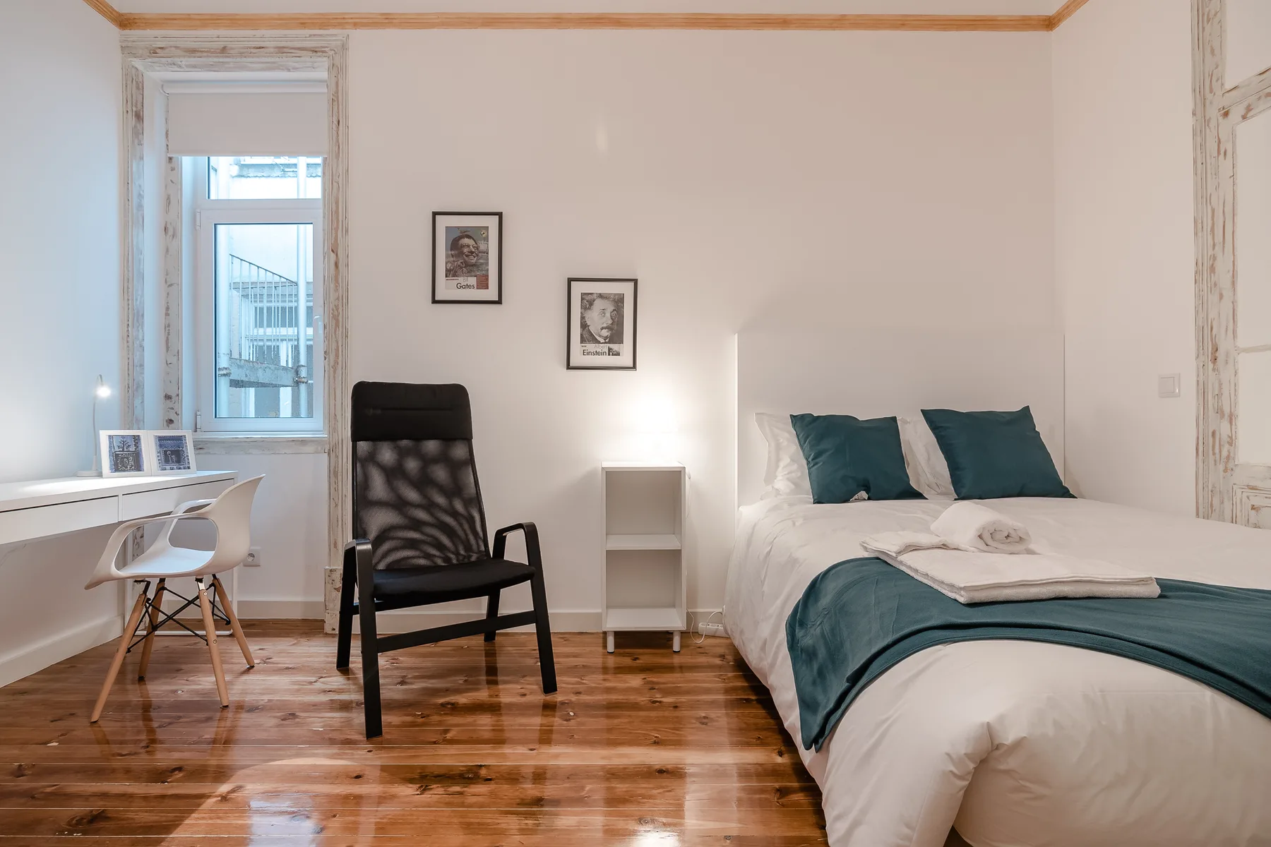 A bright bedroom with a bed, a desk, and a black chair.