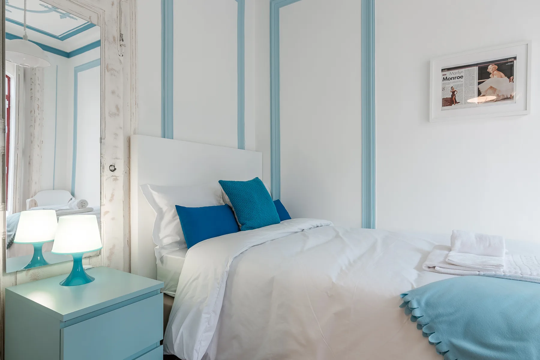 A bedroom with white bedding and blue accent pillows.