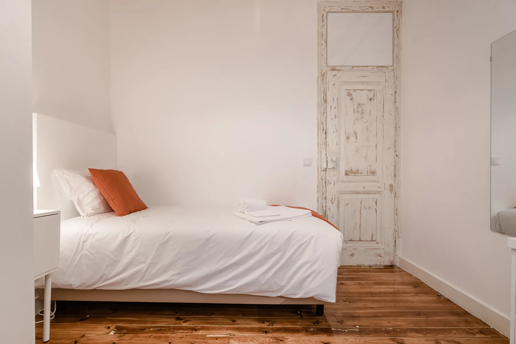 A bedroom with white bedding and an orange accent pillow.
