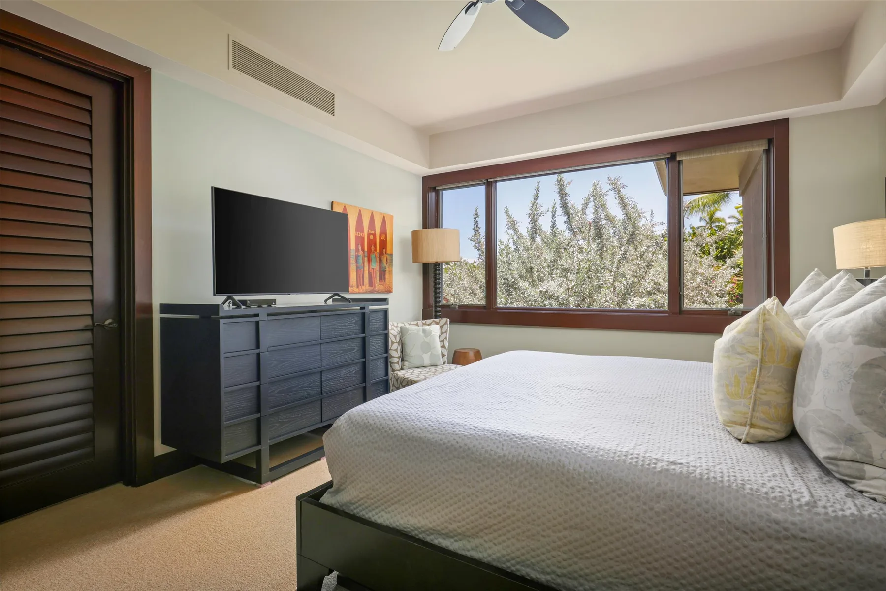 A bedroom with a large bed, a dresser, and wide windows.